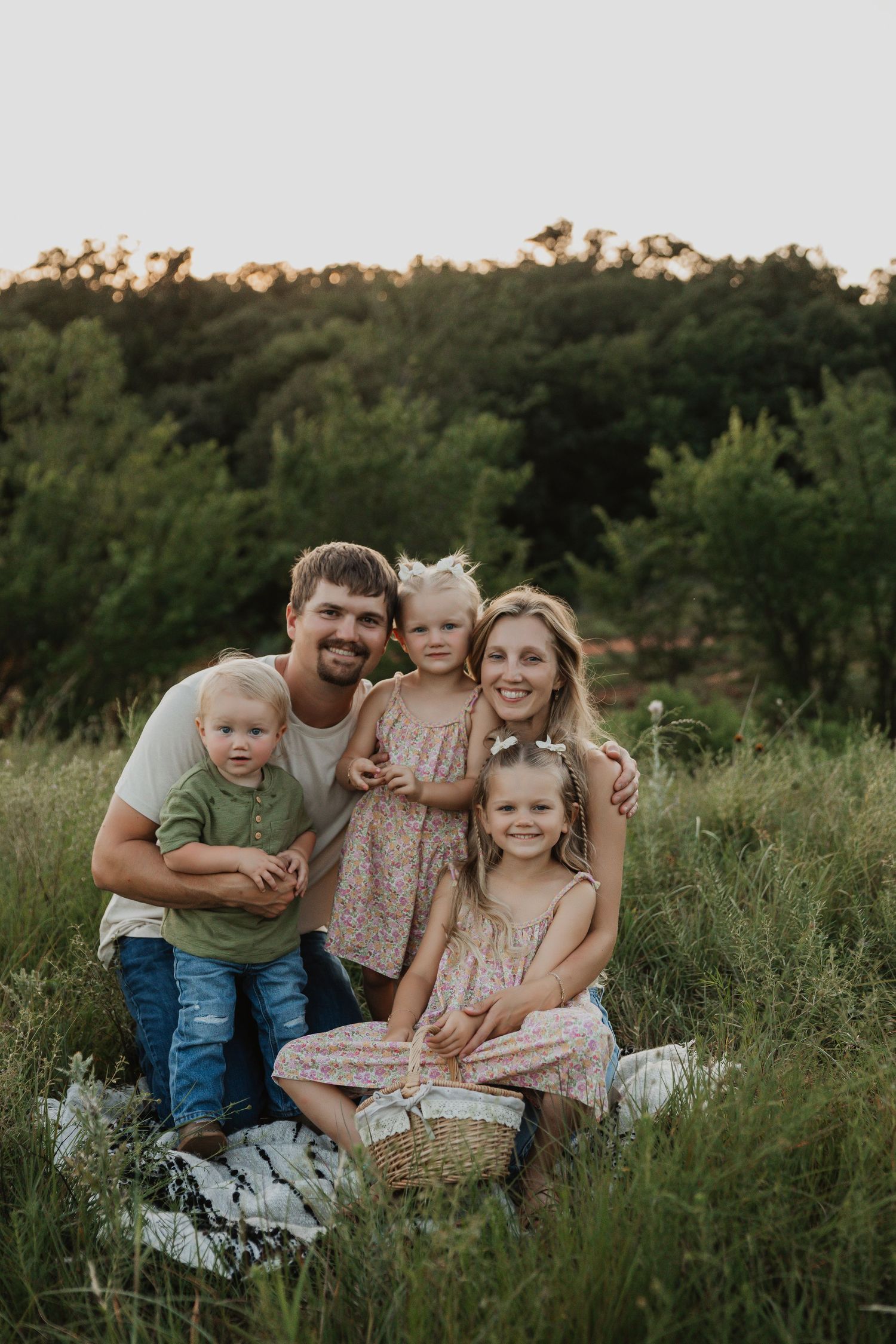 Family sitting together on a blanket in a grassy field at sunset.