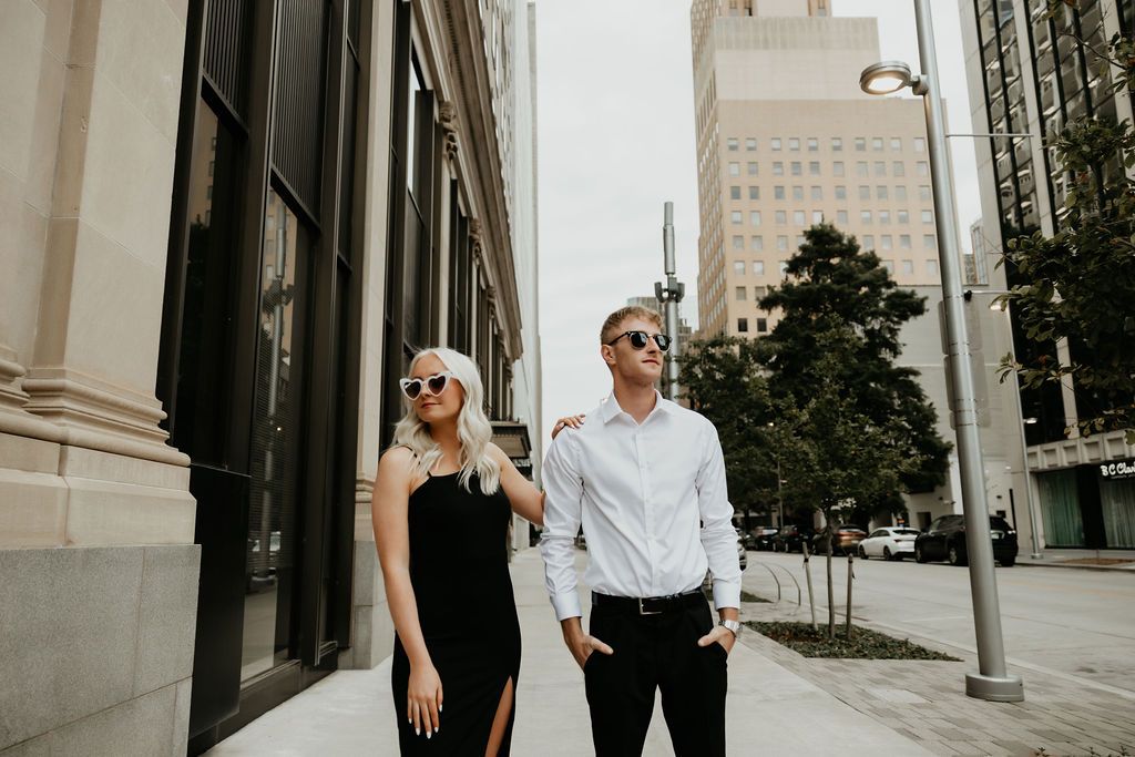 Couple in formal attire sharing intimate moments along city sidewalk.