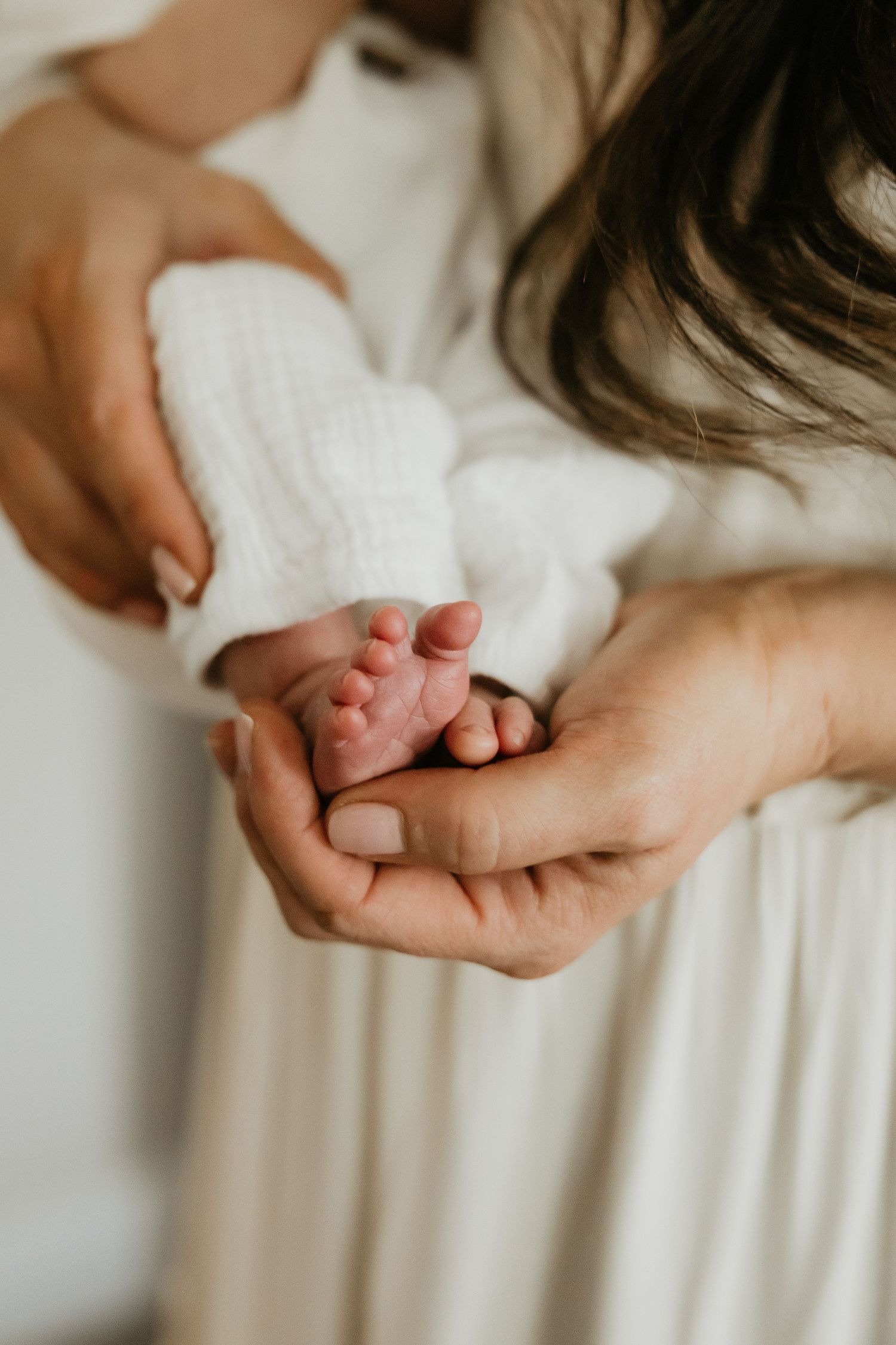Gentle hands cradle tiny newborn feet against a soft white background.