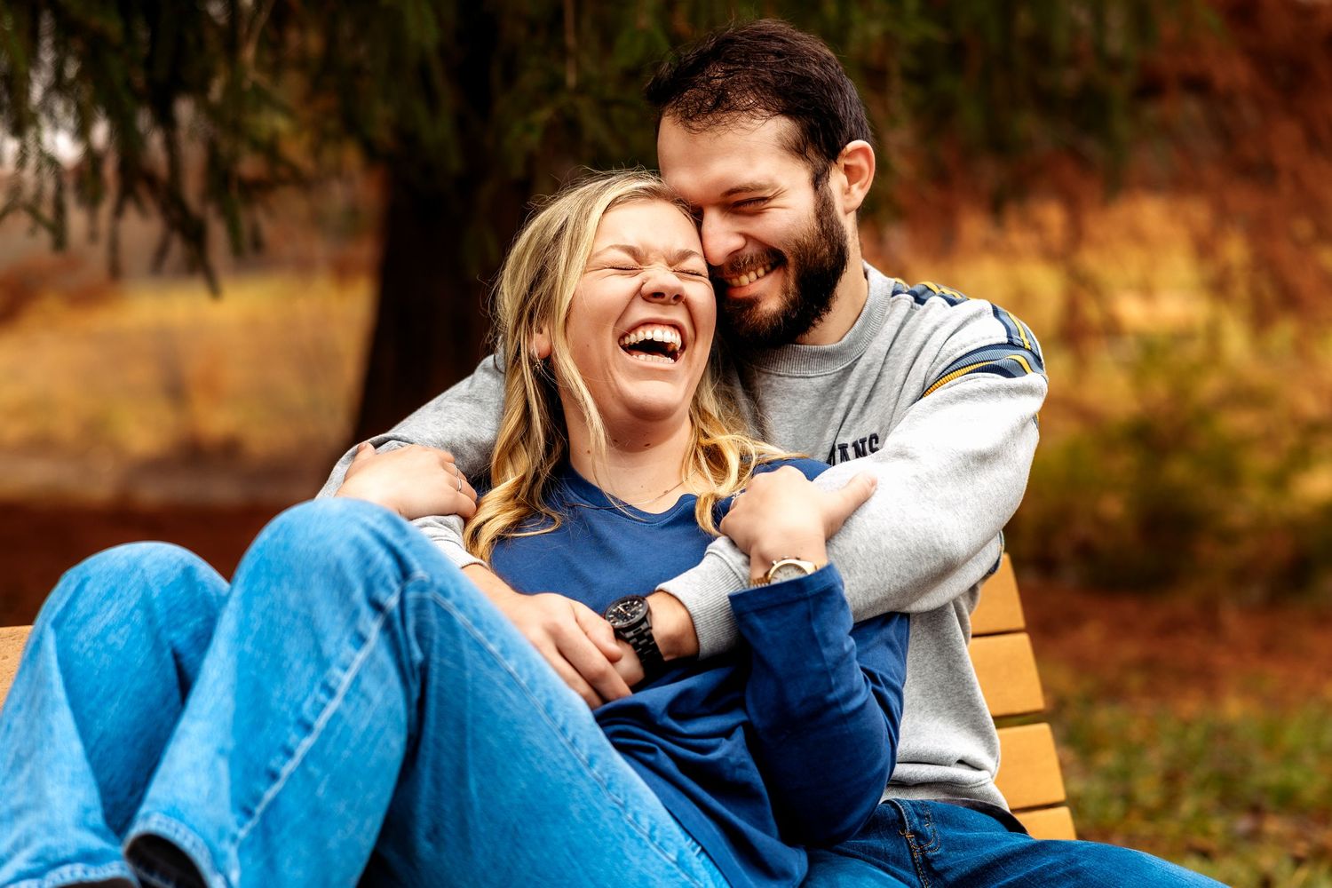 Happy couple laughing together on a bench outdoors in a park during autumn.