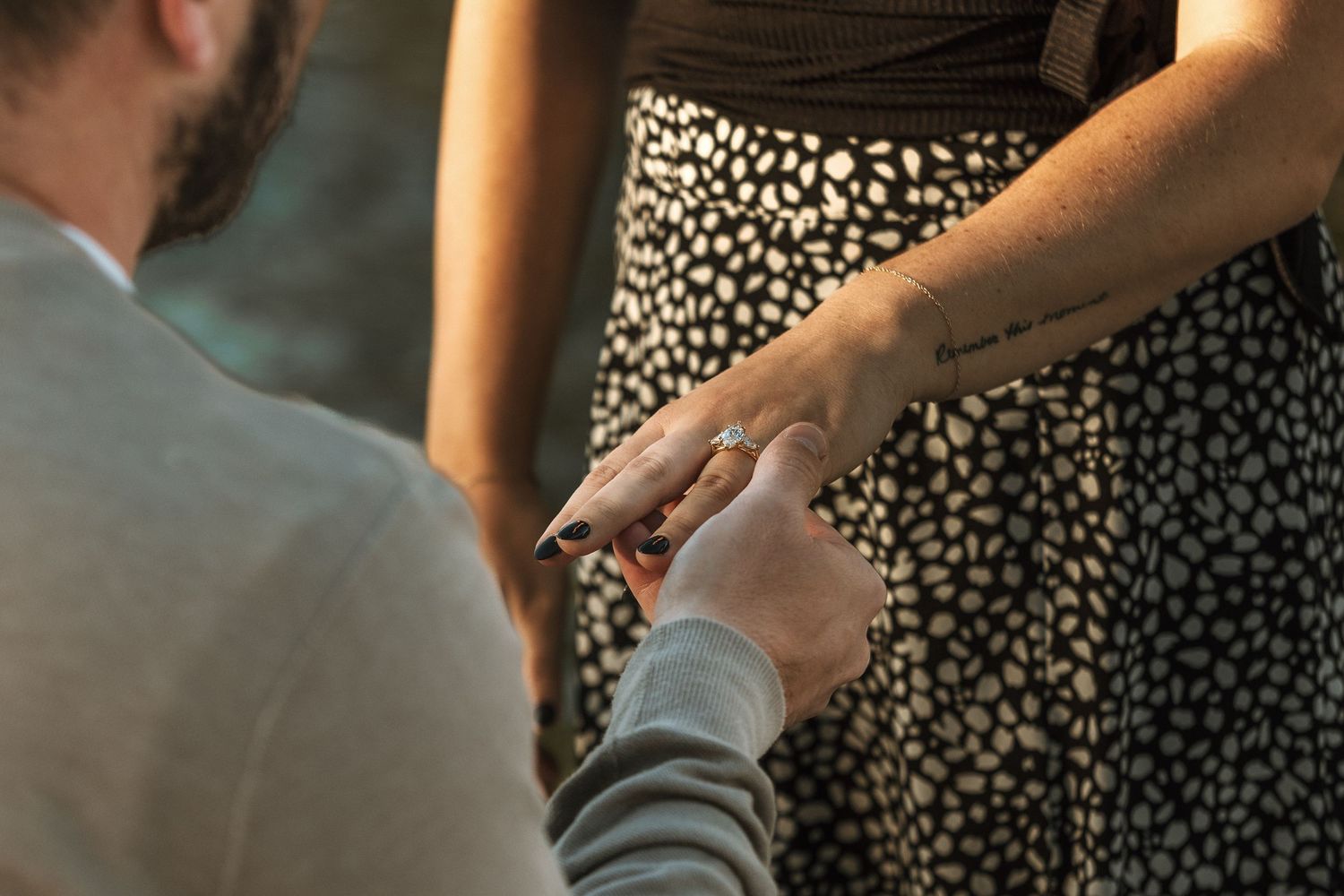 Person placing a ring on a partner's hand during a romantic proposal, wearing a floral skirt.