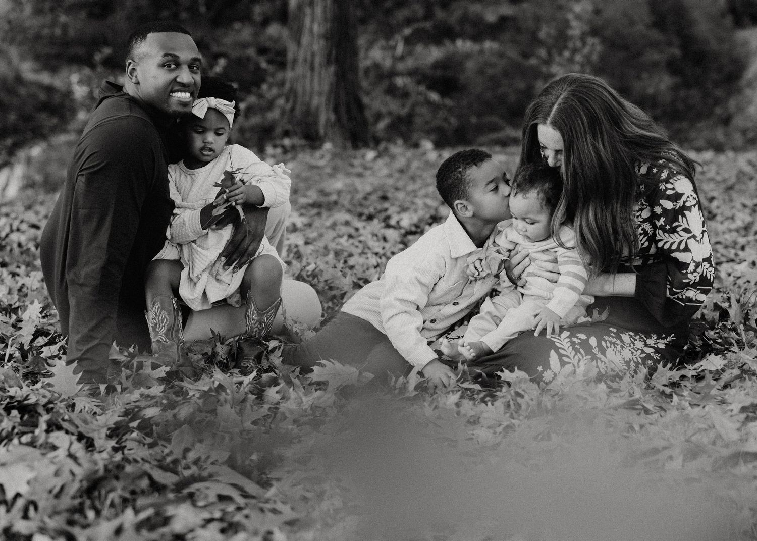 Black and white family photo of parents and three children sitting together in a lush garden setting.