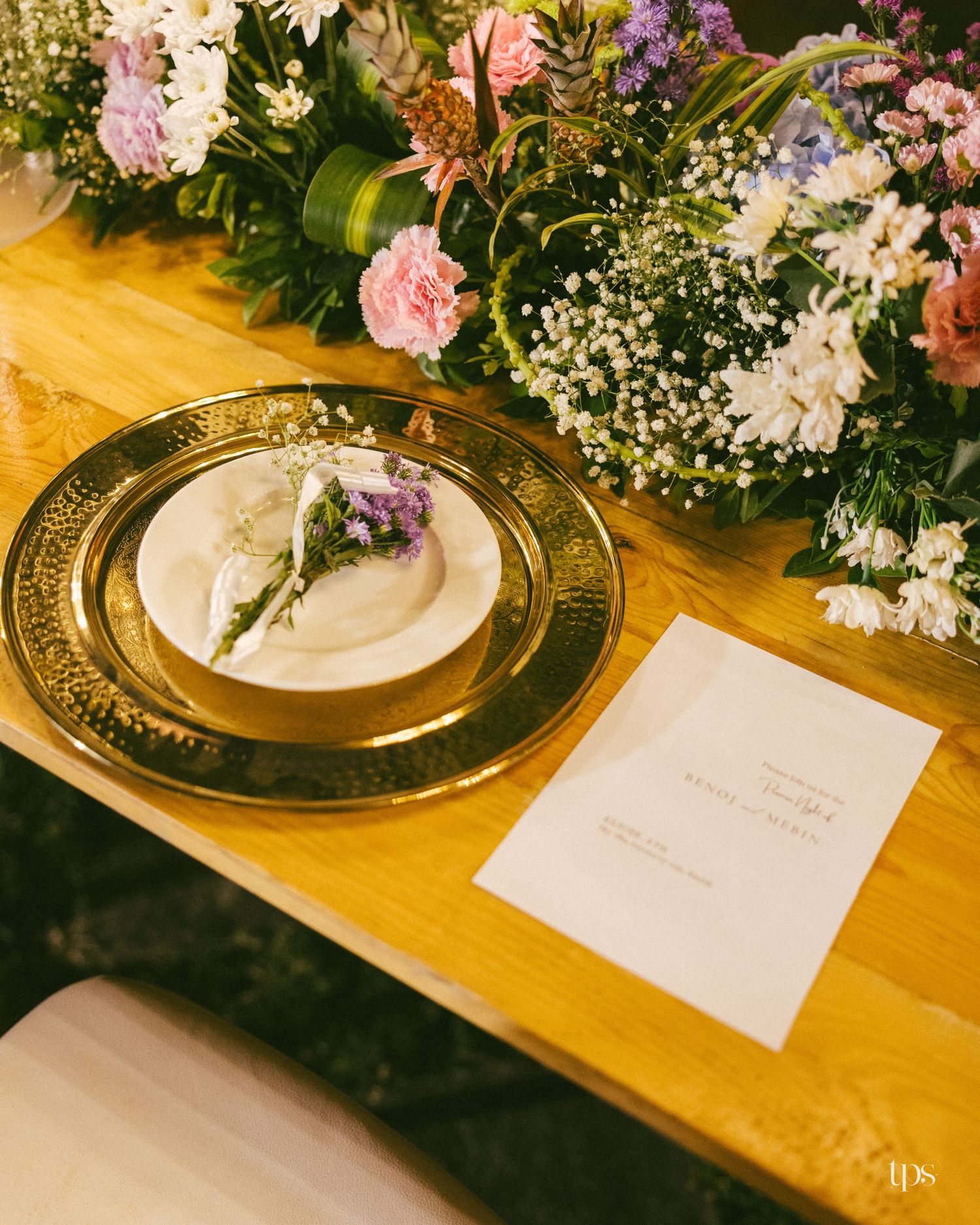 Elegant wedding table setting with a gold charger plate, white plate with lavender sprigs, printed menu card, and pastel floral centerpiece.