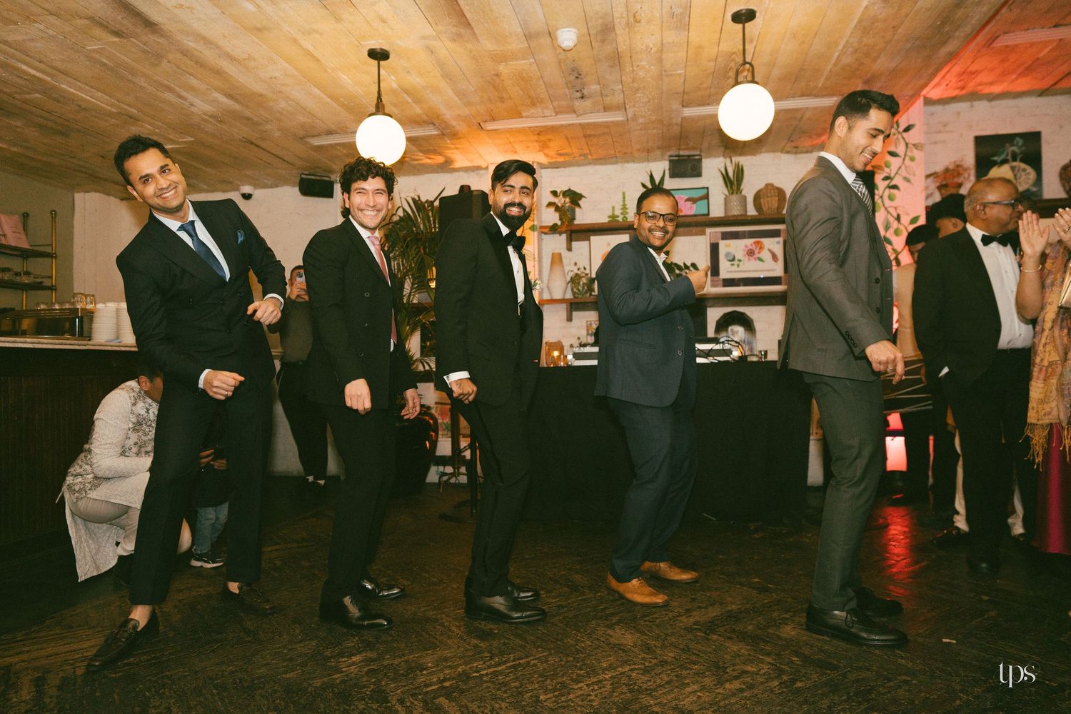 Group of men in suits dancing and celebrating at an indoor event or wedding reception party.