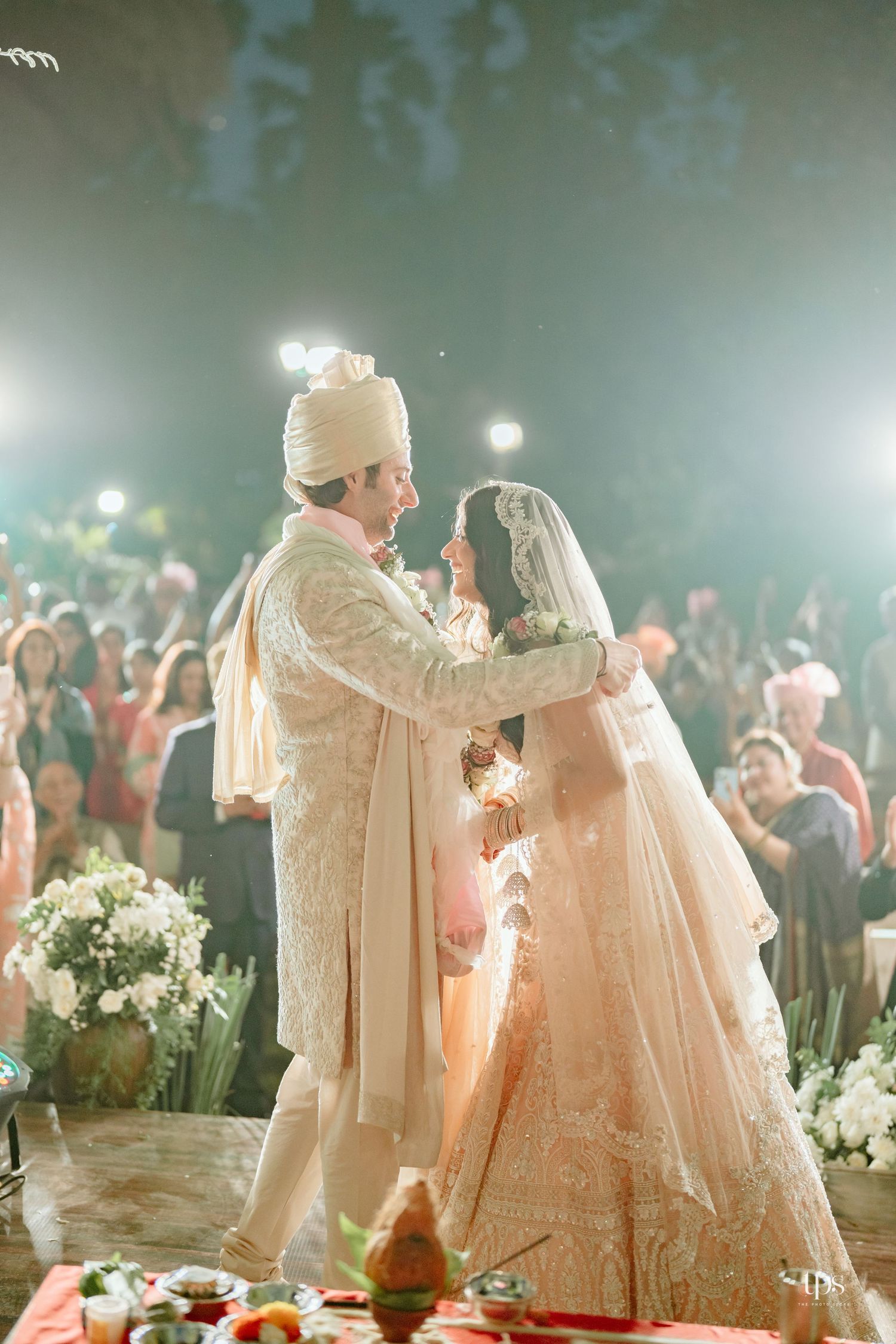 Bride and groom share a romantic moment during a traditional Indian wedding ceremony, dressed in elegant ivory outfits.