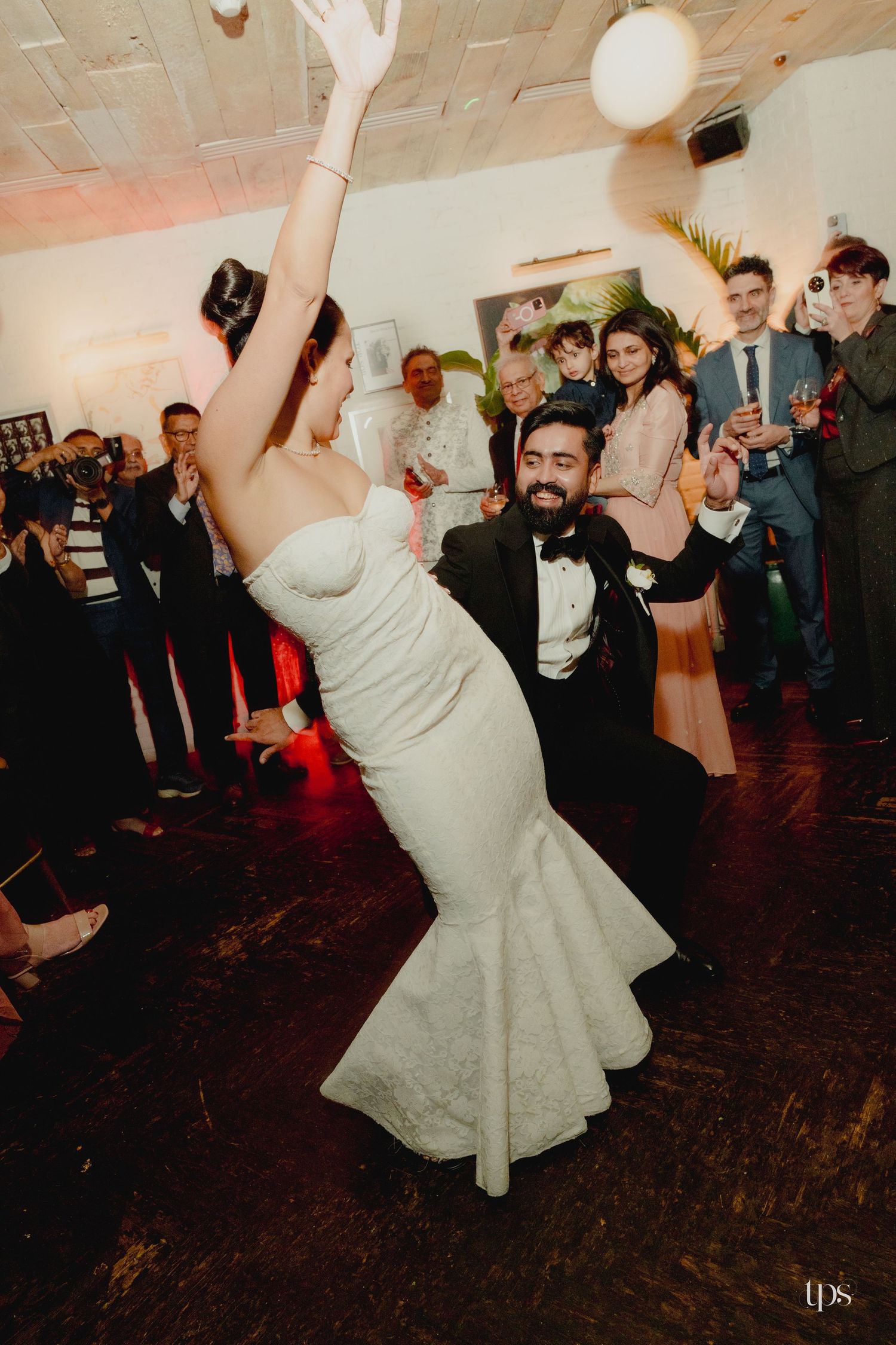 Bride and groom share a dramatic dip dance at their wedding reception surrounded by guests.