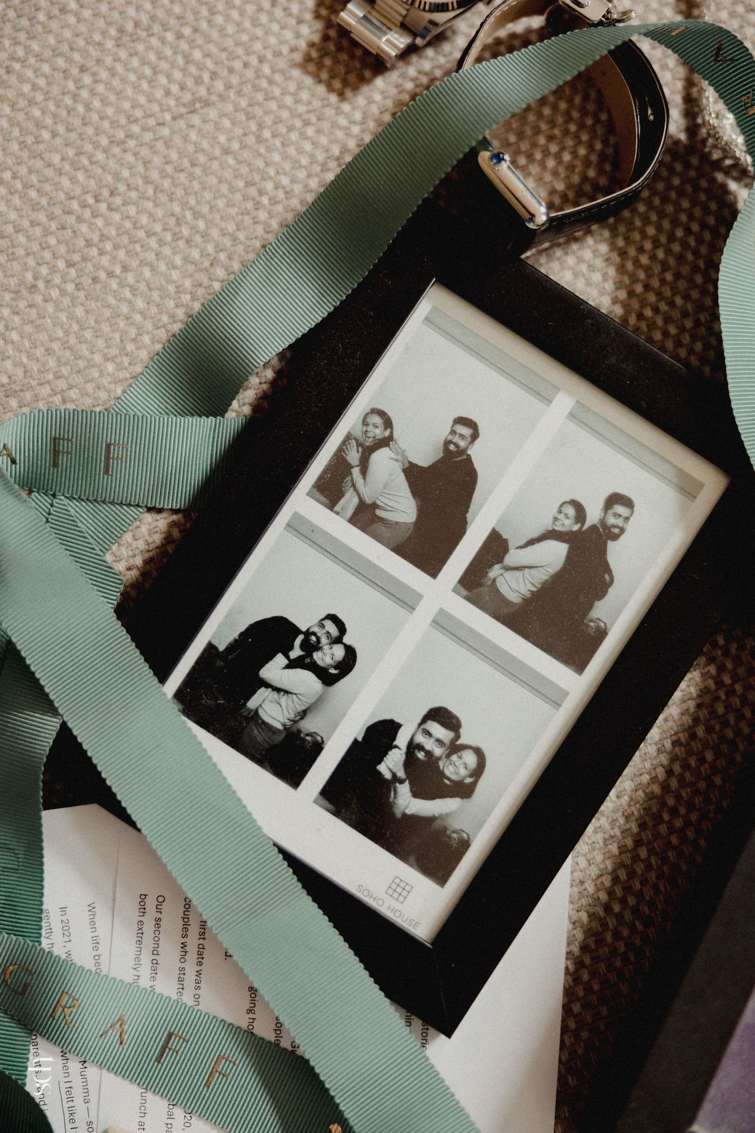 Black and white photo booth strip in a dark frame with green ribbon and belt on neutral background.