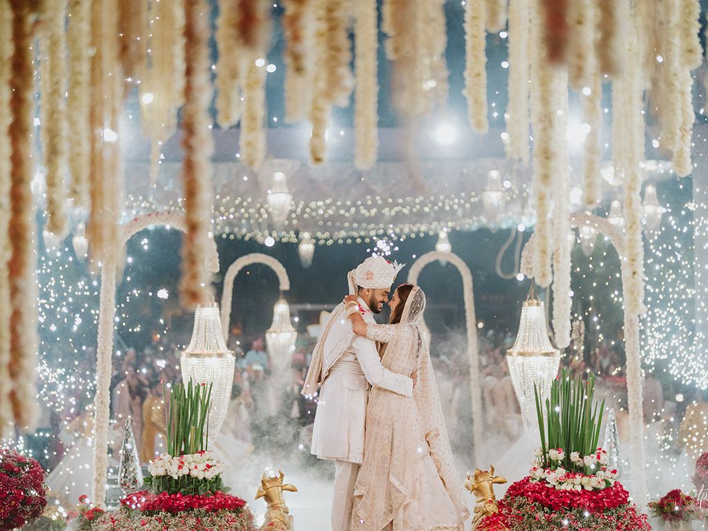 Wedding reception venue decorated with hanging lights and floral arrangements.