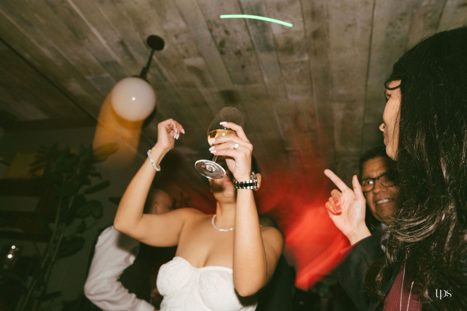 People dancing and celebrating at a lively indoor party with atmospheric red lighting and drinks.