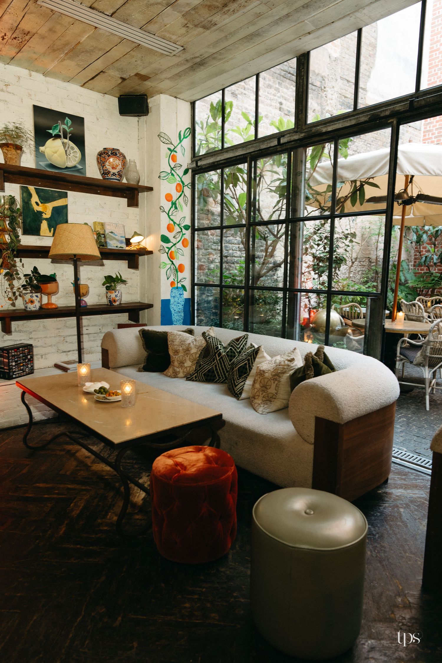 Eclectic living room with curved white sofa, industrial steel windows, wooden ceiling, and bohemian decor accents.