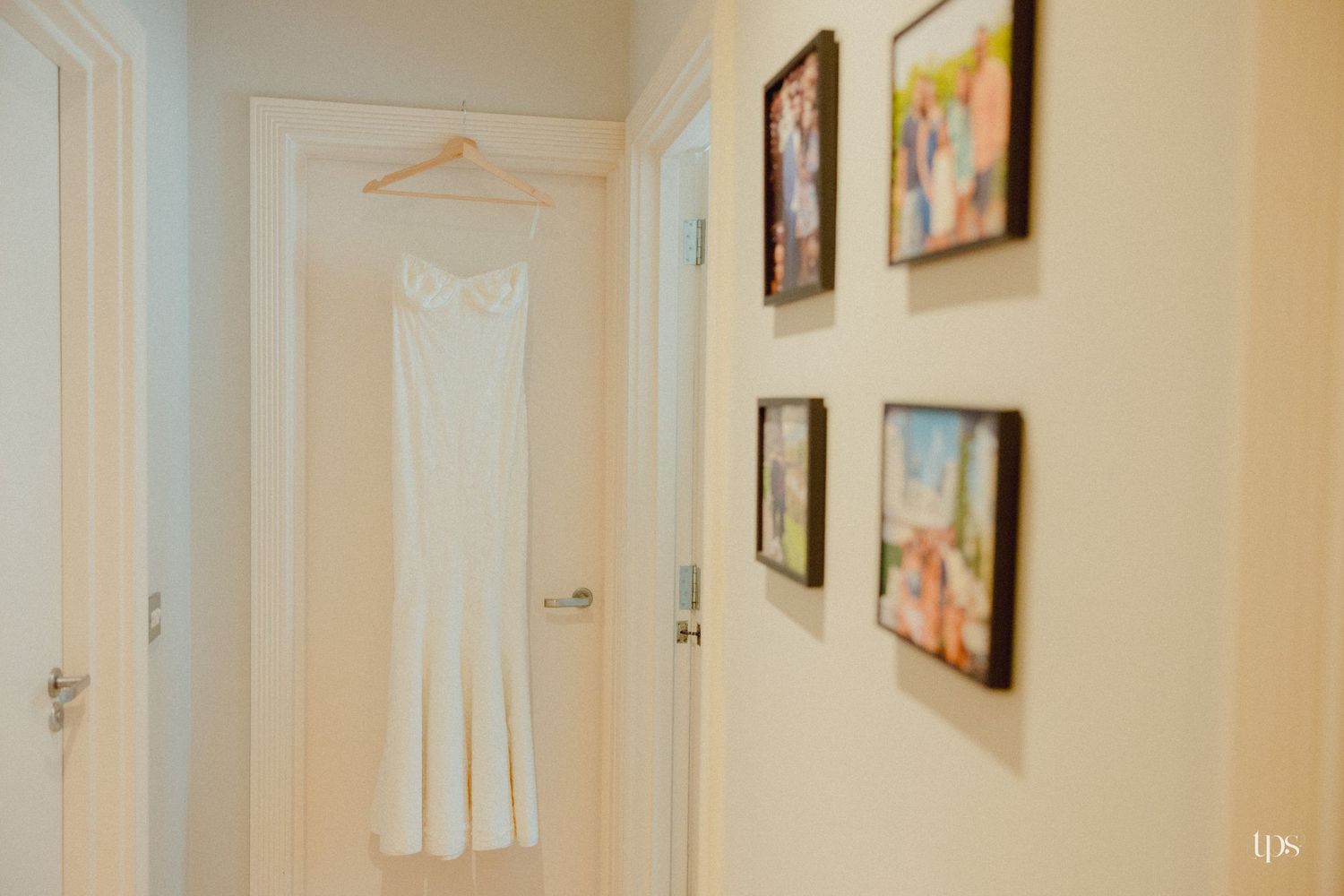 A white wedding dress hanging in a hallway with framed photos on the wall.