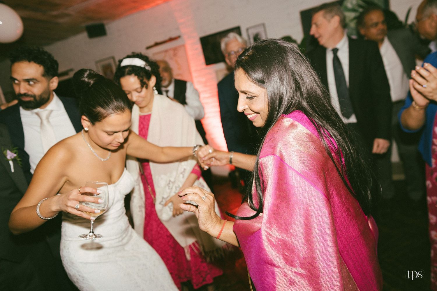 Two women in elegant attire share a joyful dance moment at an indoor wedding reception celebration.