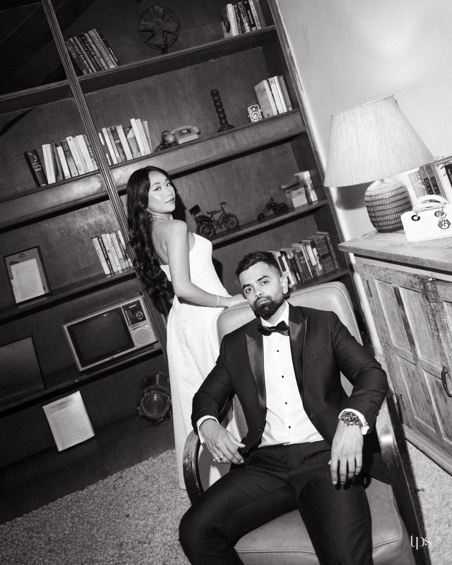 Black and white portrait of a bearded man in a tuxedo seated in a leather chair beside a woman in a white gown in a vintage study.