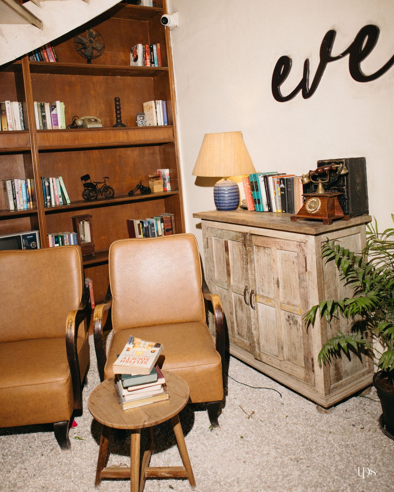 Cozy lounge corner with two tan leather armchairs, a wooden bookshelf, a rustic cabinet with a vintage telephone, lamp and a potted plant.