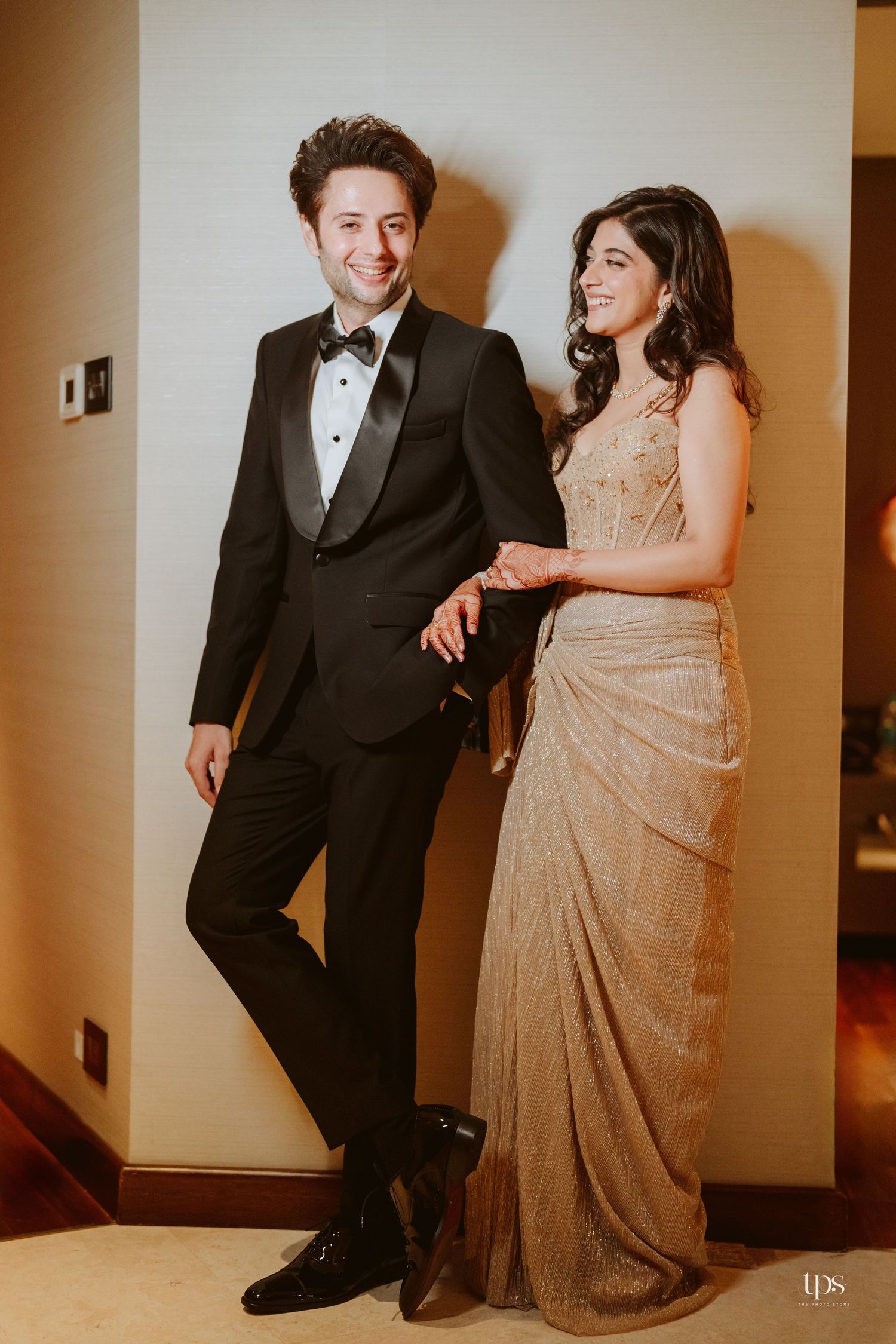 Elegant couple posing together, man in black tuxedo and woman in gold saree, at a formal event.