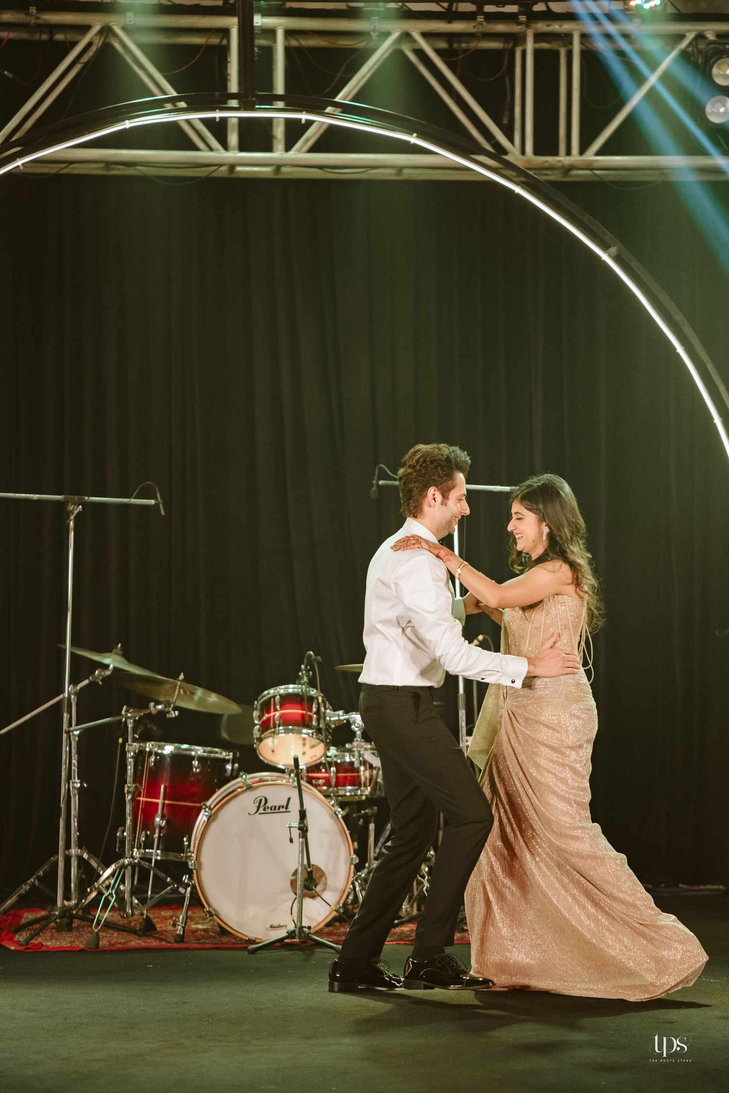 Couple sharing a romantic first dance on stage with a Pearl drum kit and circular arch backdrop at a wedding reception.