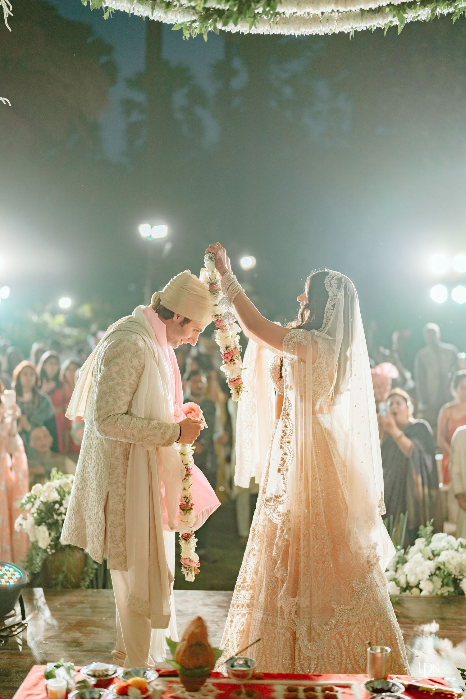 Bride and groom exchange floral garlands during a traditional Indian wedding ceremony at an elegant outdoor night venue.