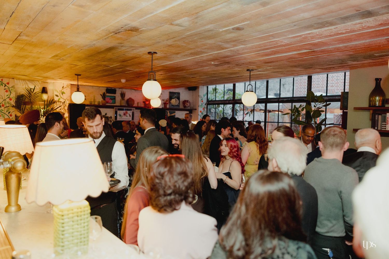 Crowded indoor bar event with warm lighting, wood ceiling, and guests mingling in a cozy restaurant setting.