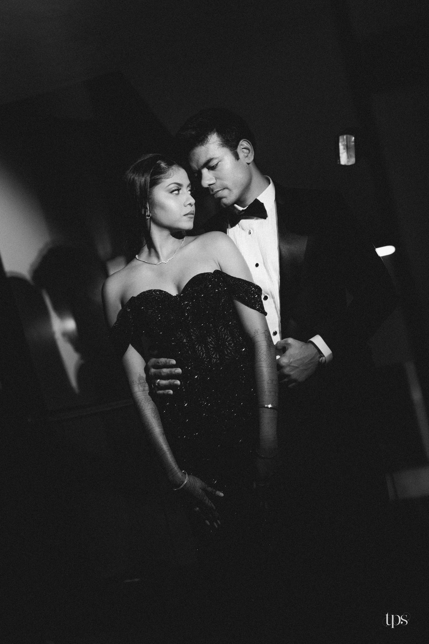 Black and white photo of an elegant couple in formal attire sharing an intimate moment at a glamorous event.