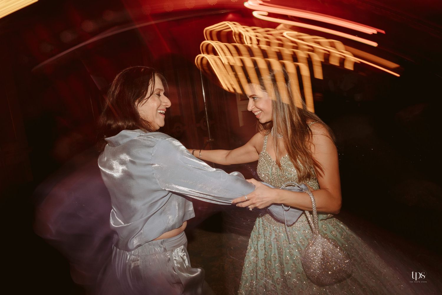 Two women joyfully dancing together at a wedding reception with colorful neon lights in the background.