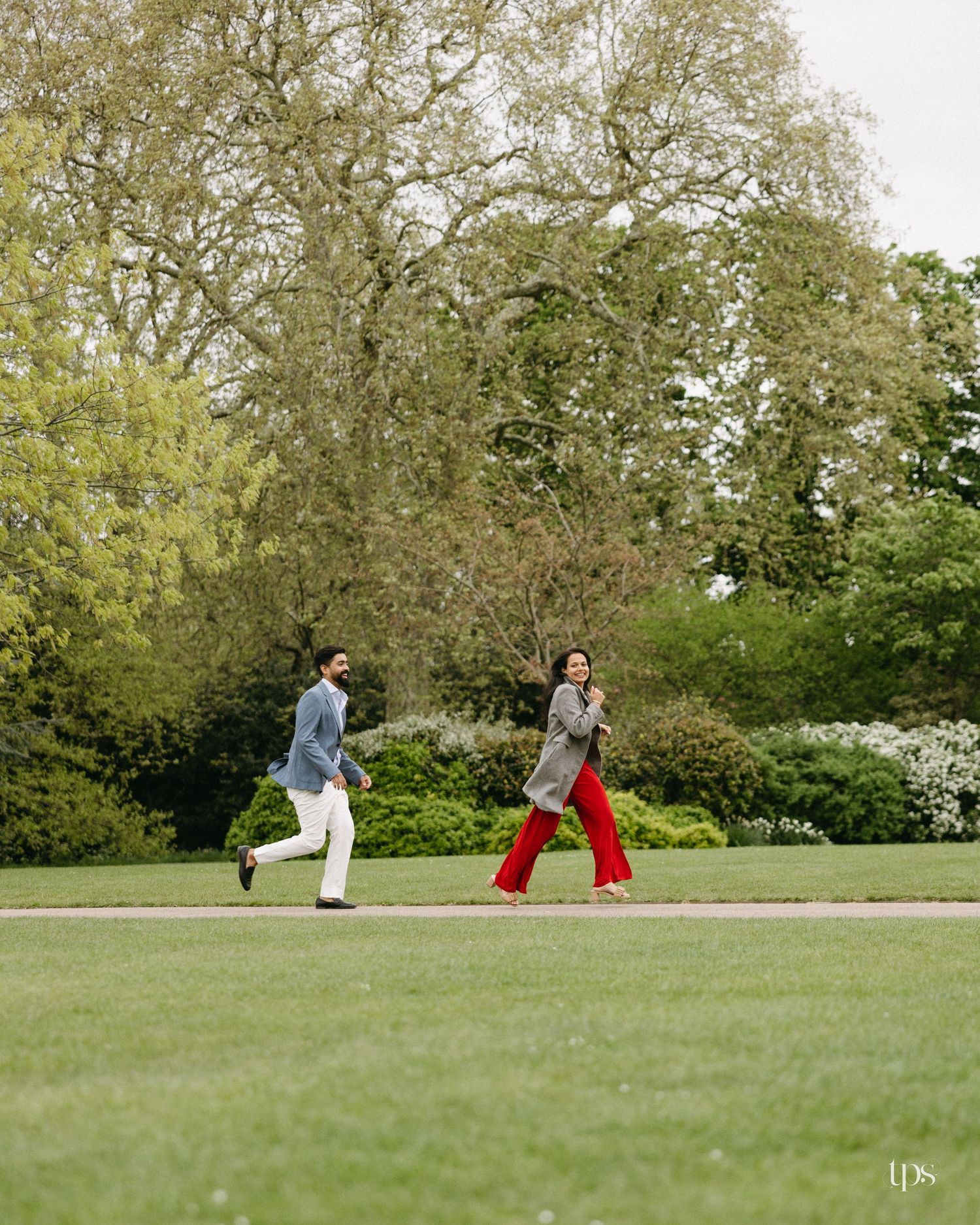 Couple playfully running on lush green lawn surrounded by blooming trees in a scenic park during spring.