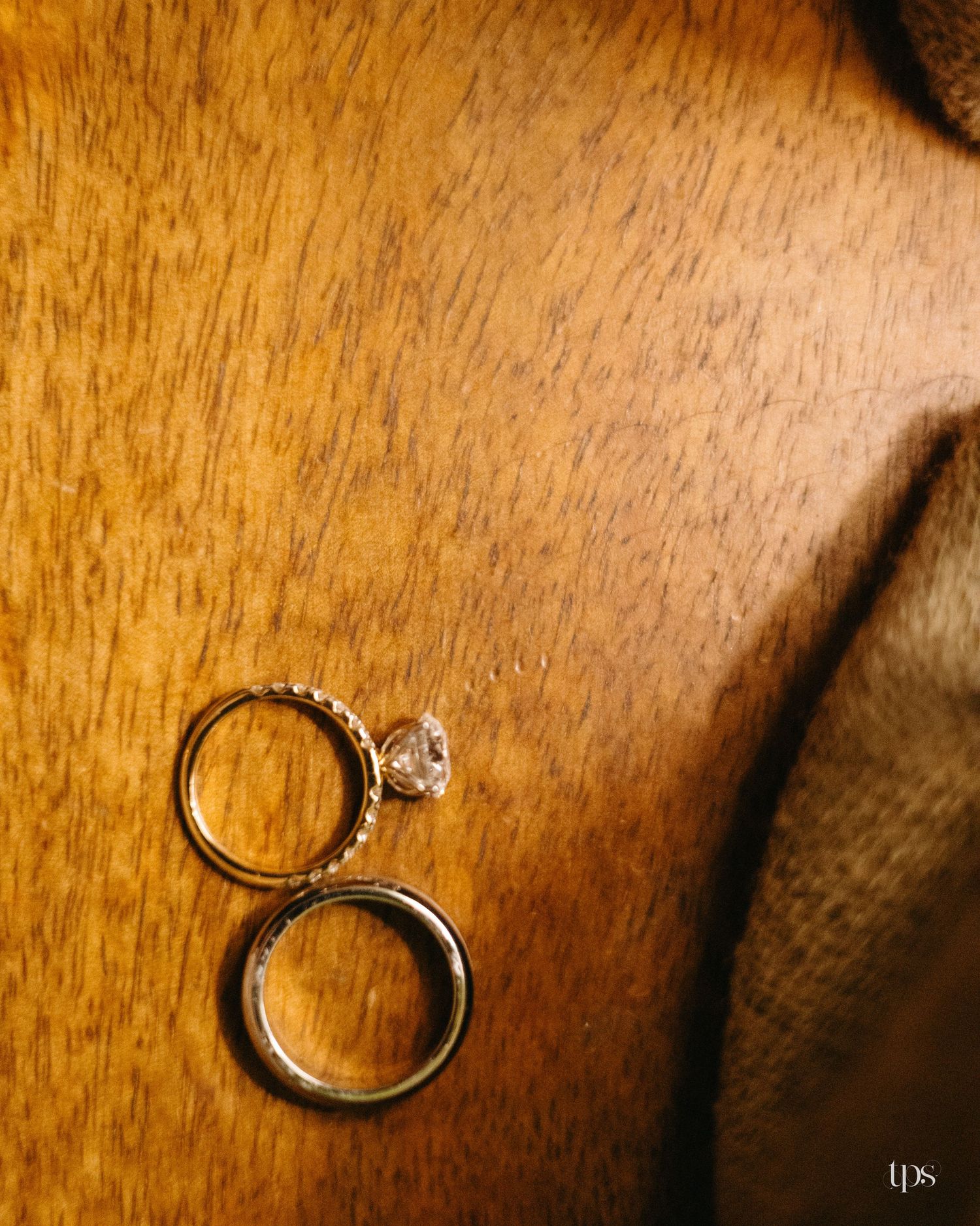 Diamond engagement ring and plain wedding band resting on a warm wooden surface beside a textured burlap fabric.