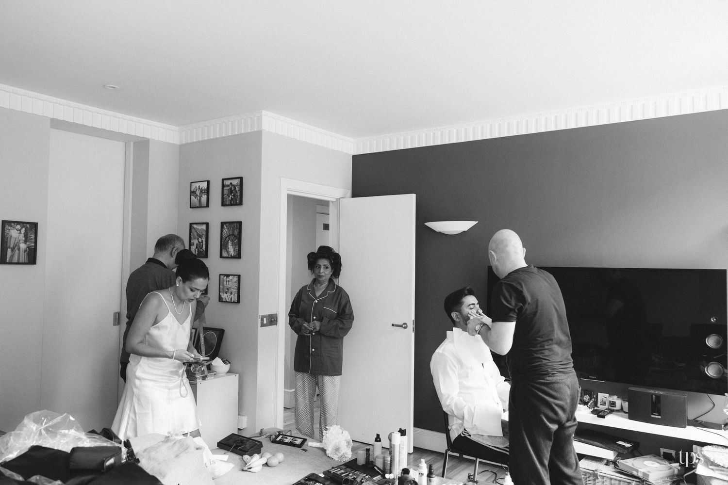 Black and white photo of bridal party getting ready, with makeup and hair being done in a hotel room.