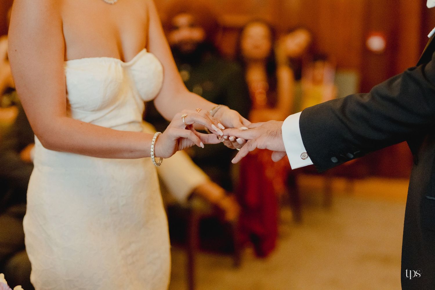 Bride and groom exchanging rings during wedding ceremony, guests seated in background.