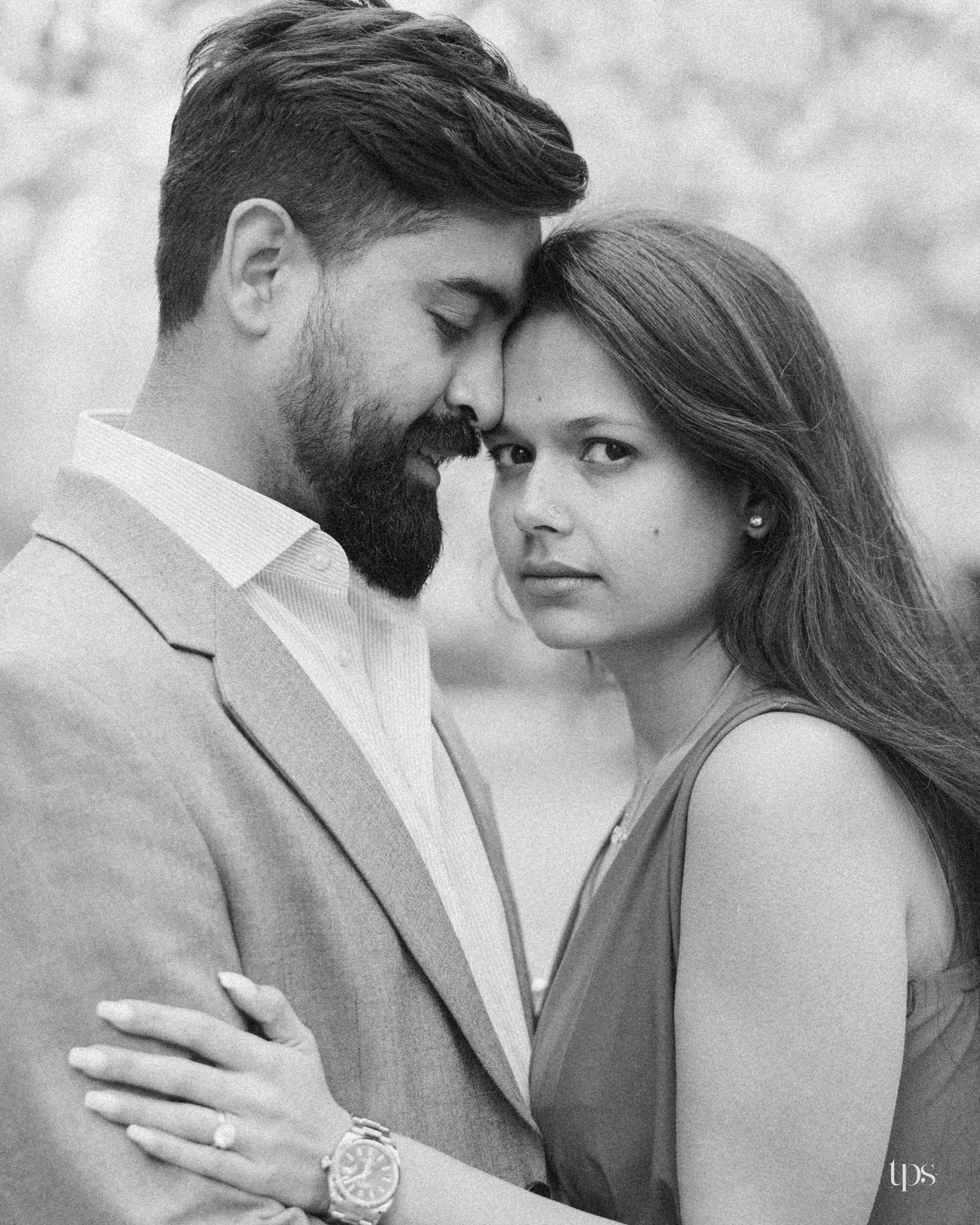 Black and white photo of a bearded man in a suit embracing a young woman, foreheads nearly touching in a romantic pose.