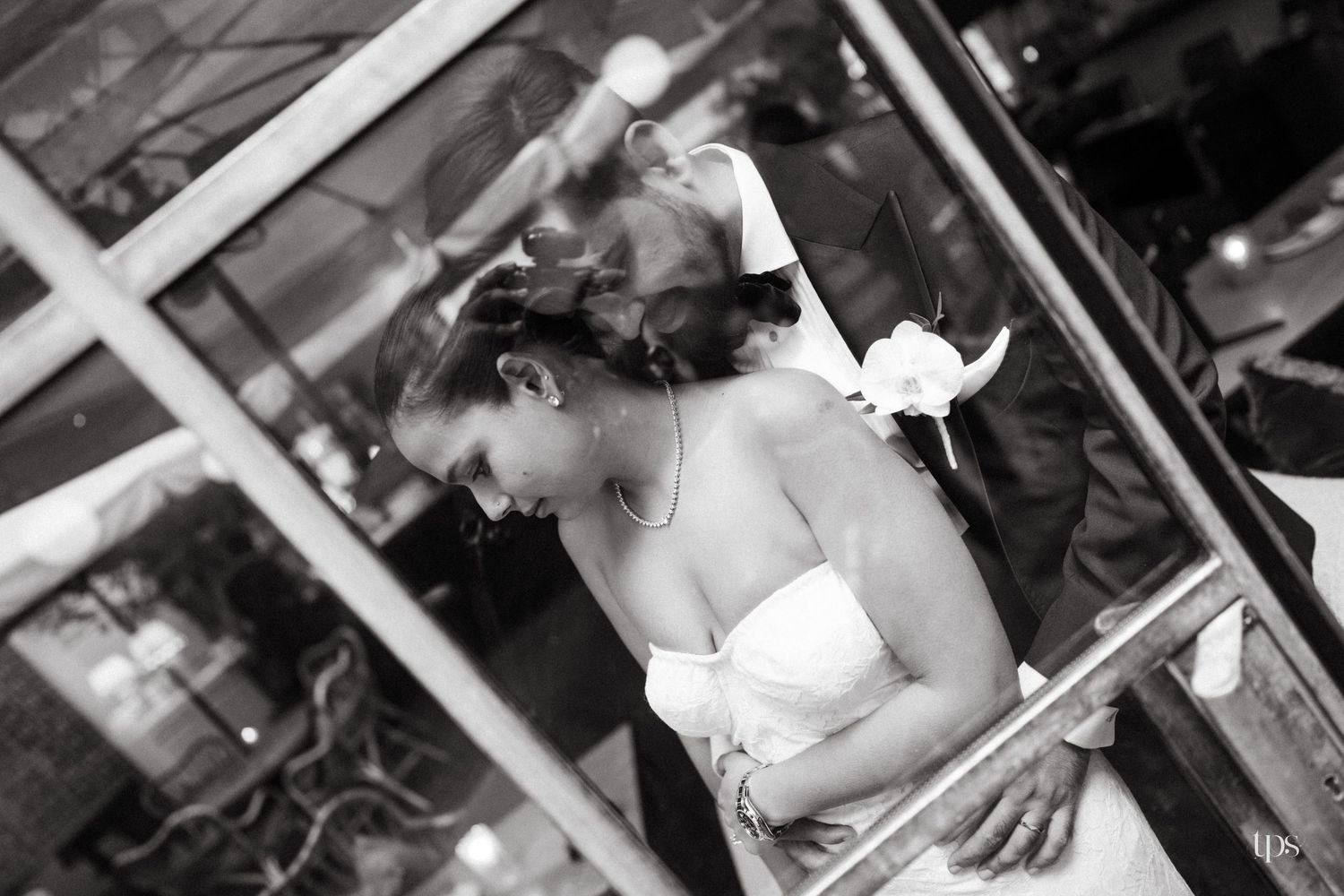 Black and white photo of a bride in a strapless gown leaning forward, captured through a glass reflection.
