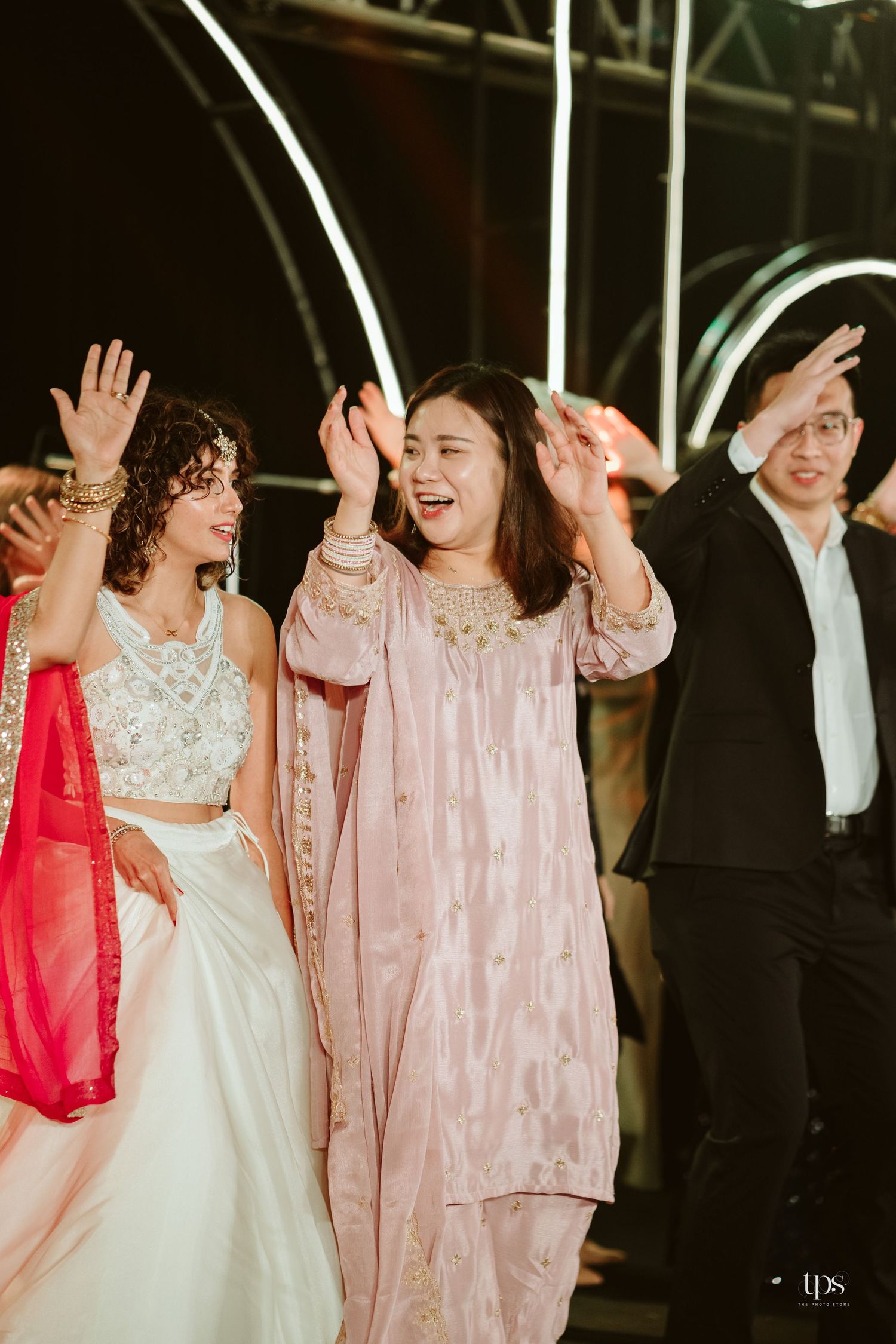 Women in traditional Indian attire dancing joyfully at a festive wedding celebration event.