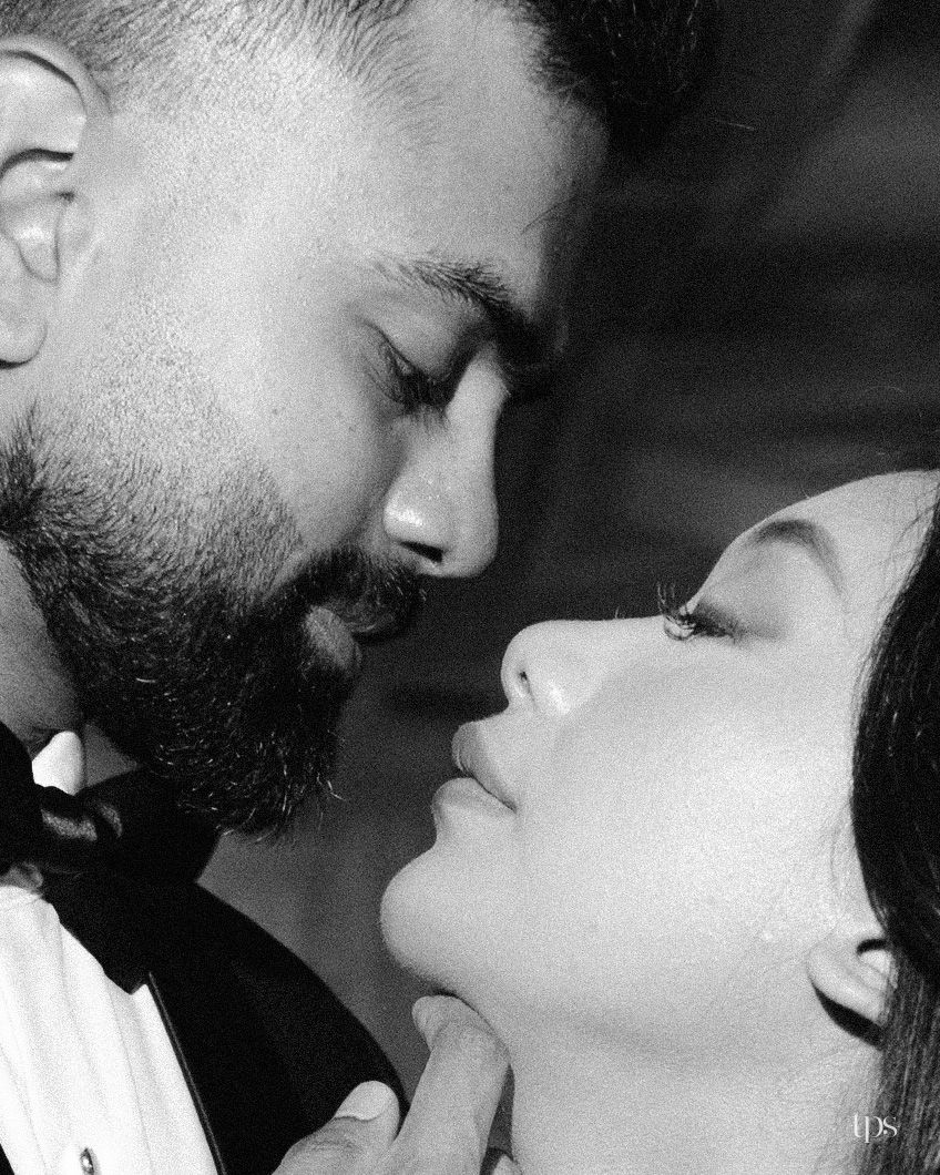 Black and white close-up of a bearded groom in a tuxedo and bow tie leaning in to kiss his bride, his hand gently lifting her chin.