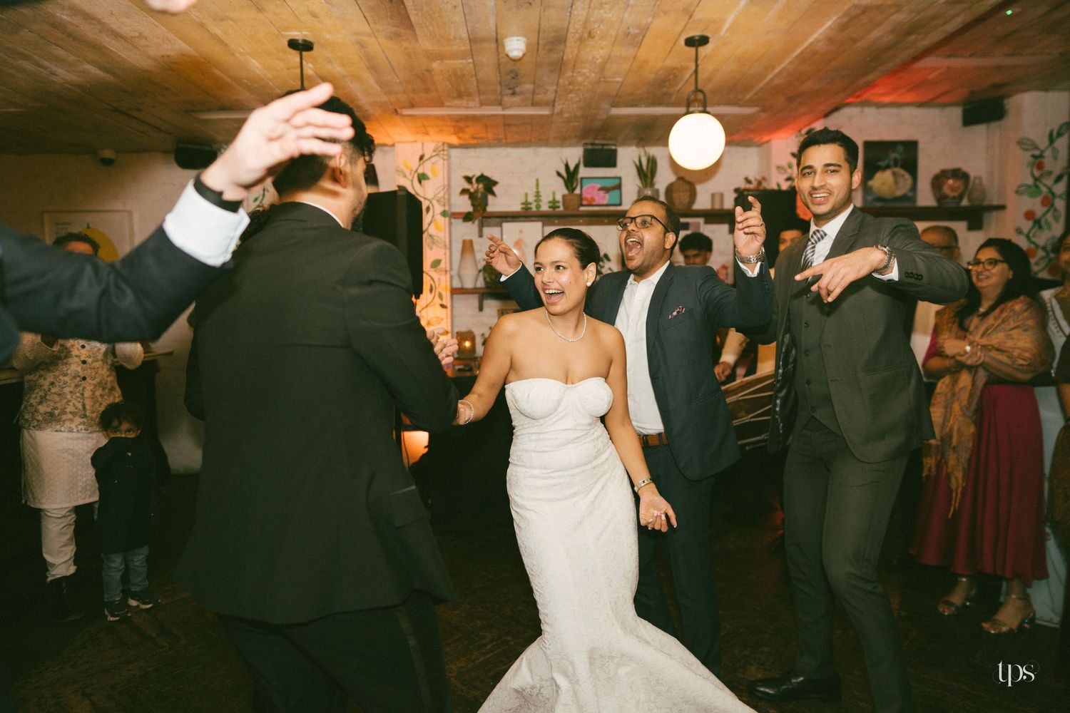 Bride in white gown dances joyfully with groom in gray suit at lively wedding reception celebration.