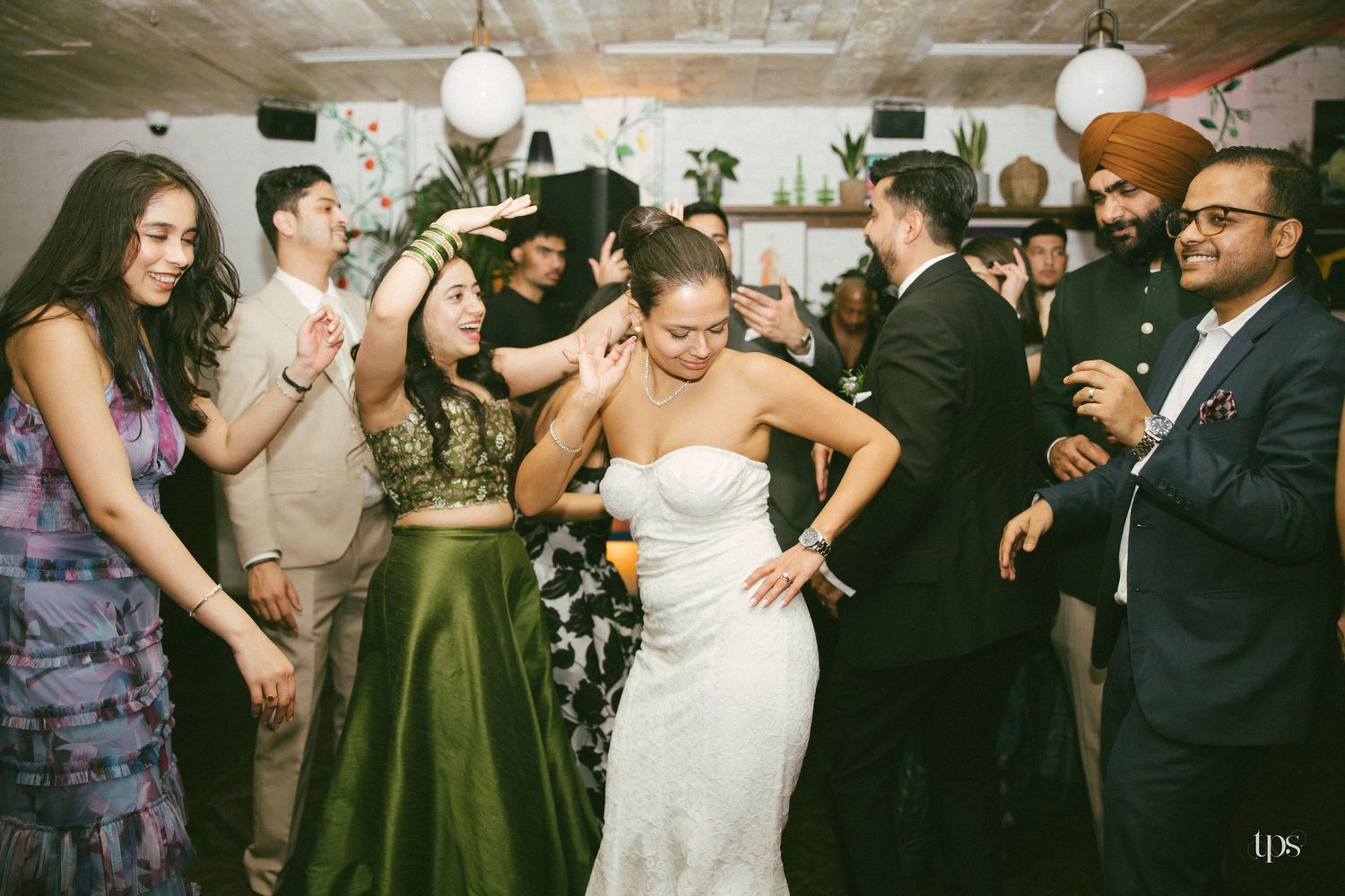 Bride in white strapless gown dancing joyfully with guests at a lively wedding reception party.