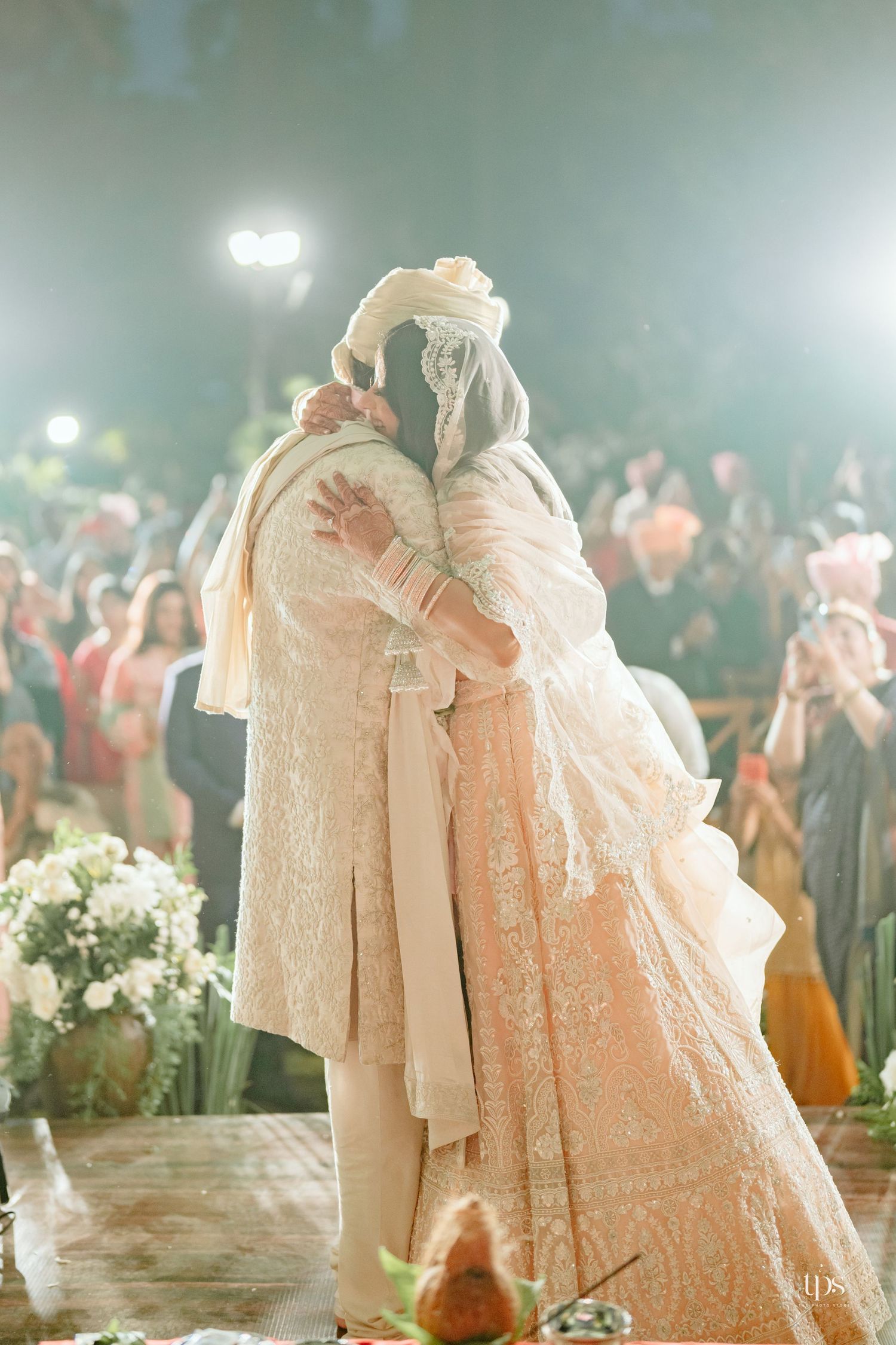 Bride and groom share a heartfelt embrace during an Indian wedding ceremony, wearing elegant cream and peach traditional attire.