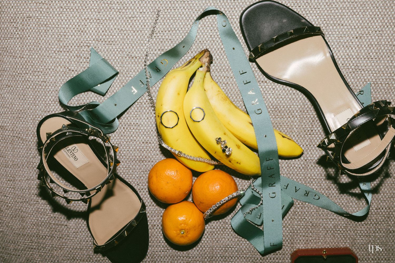 Flat lay of bananas, oranges, measuring tape, and black strappy sandals on a gray surface.