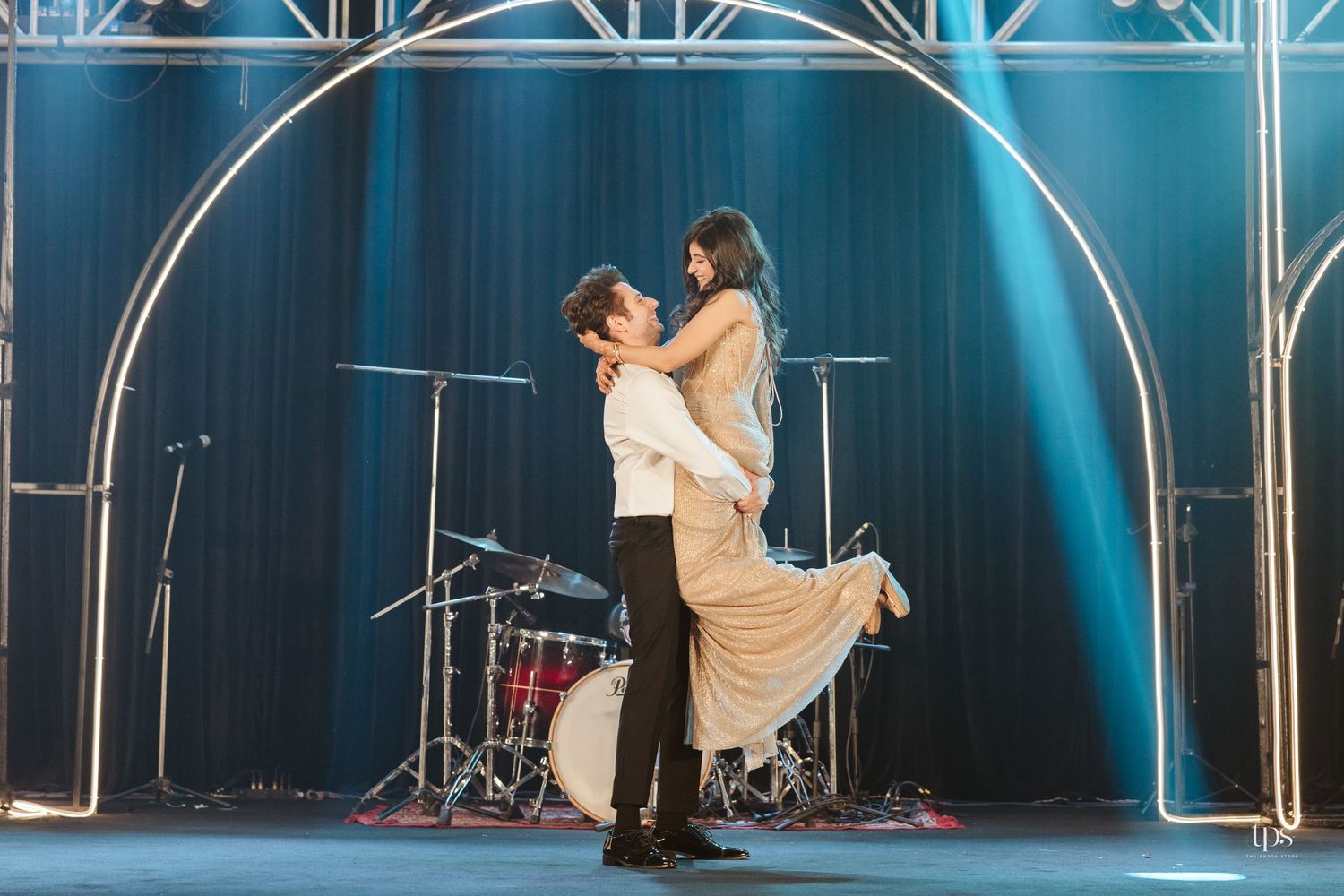 Couple sharing a romantic dance lift on stage with blue lighting and drums in the background.