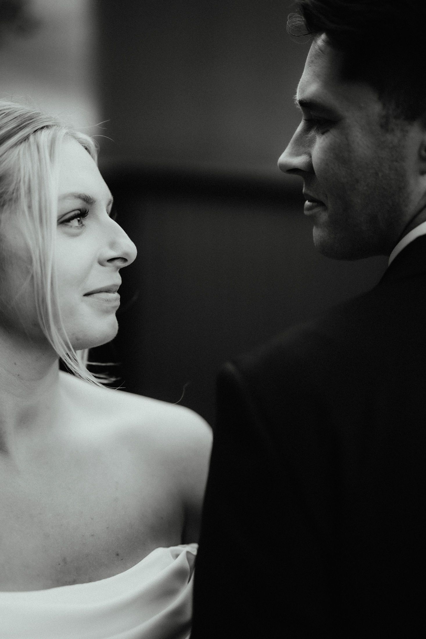 Black and white close-up portrait of a bride and groom in profile smiling at each other during their wedding photoshoot.