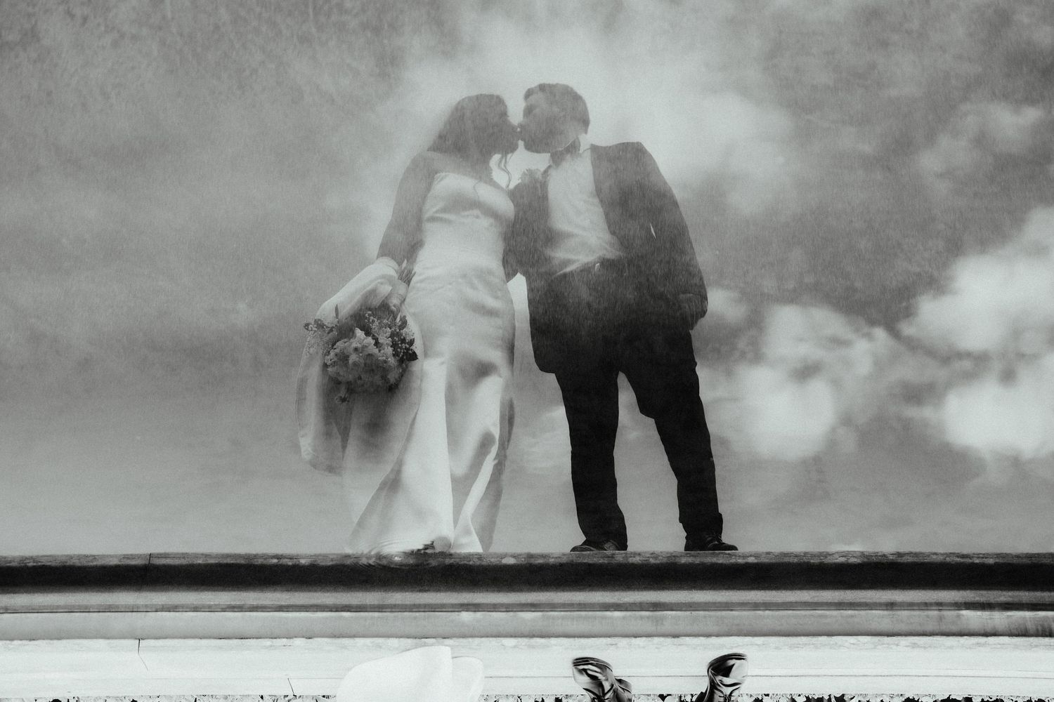 Black and white photo of a bride and groom sharing a romantic kiss outdoors on their wedding day.