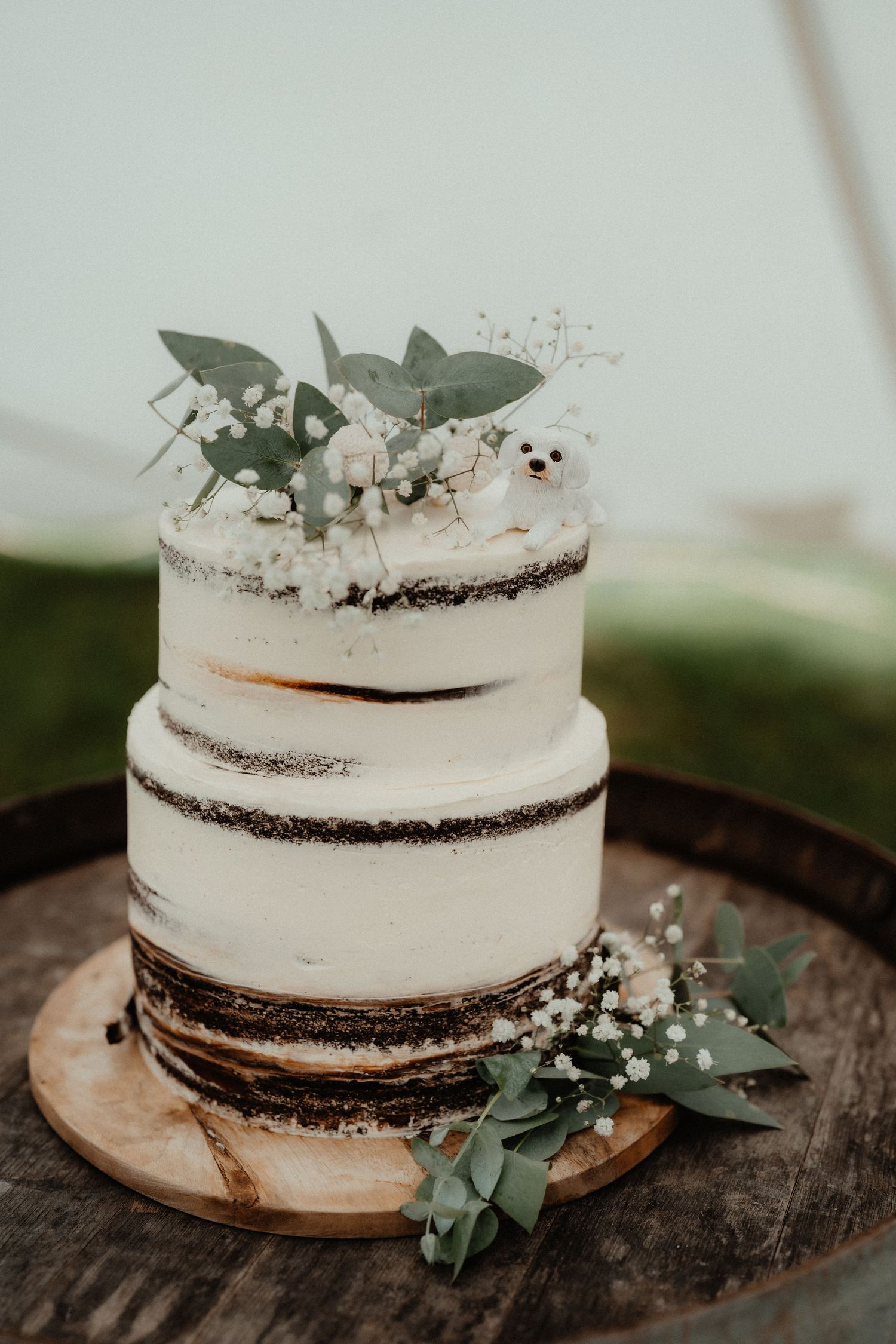Rustic two-tier semi-naked wedding cake topped with eucalyptus, baby's breath and a small polar bear figurine on a wooden barrel.