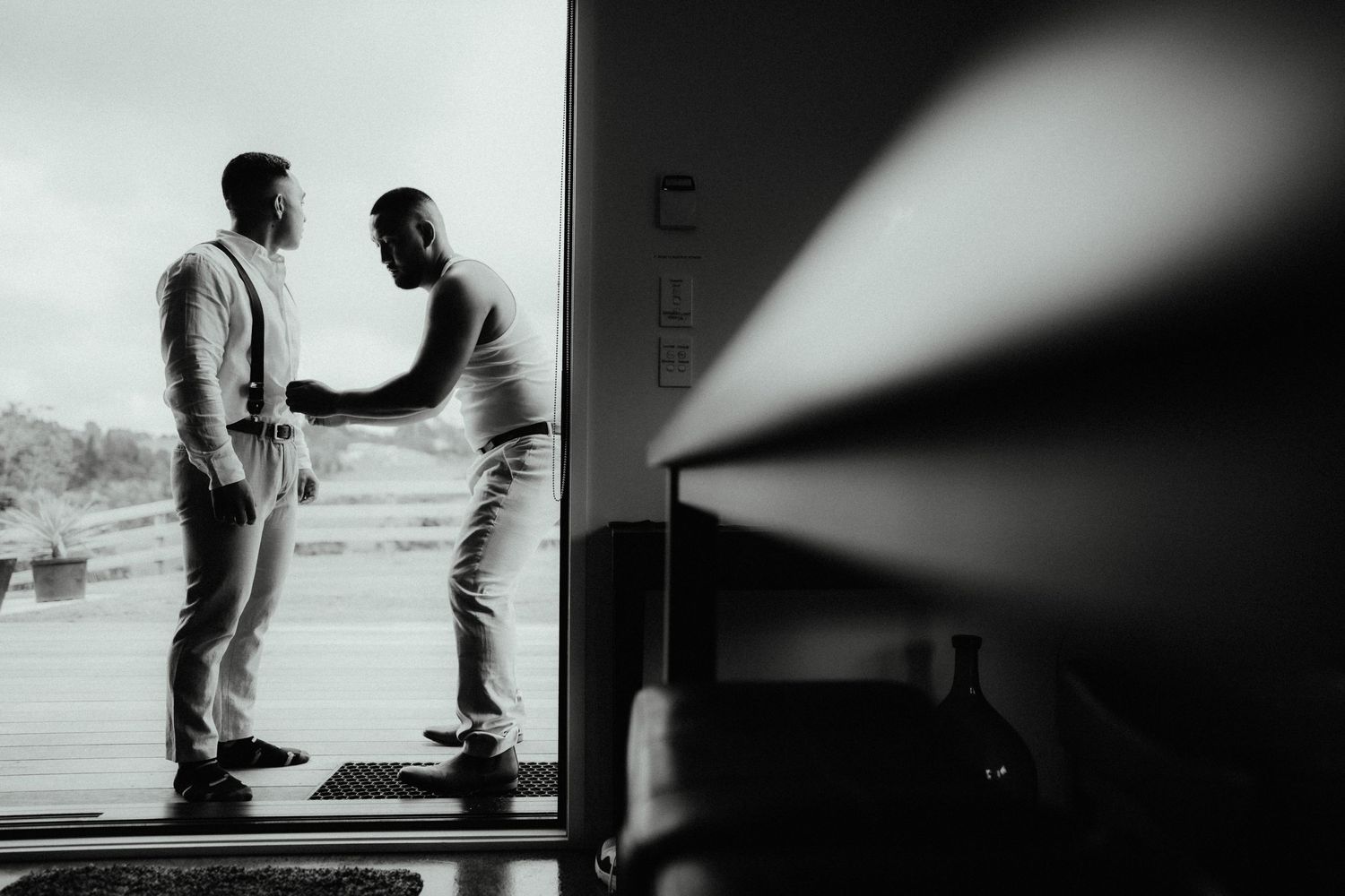 Black and white photo of two groomsmen sharing a handshake in a bright doorway while getting ready for the wedding day.