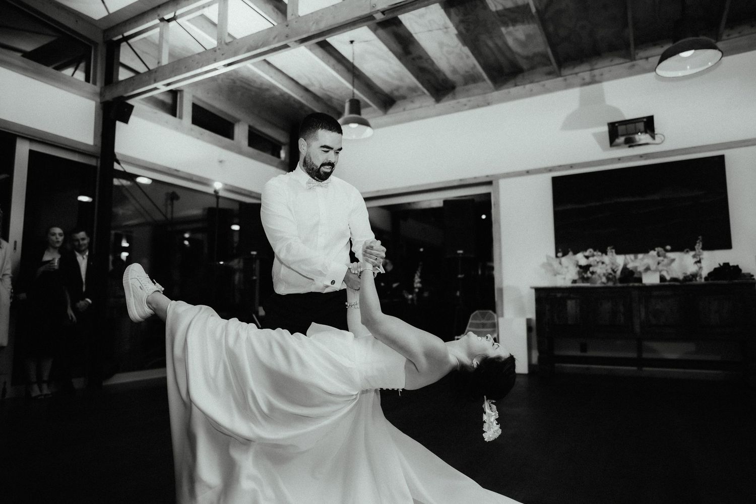 Black and white photo of a groom dipping his bride in a dramatic dance move on the dance floor at a wedding reception.