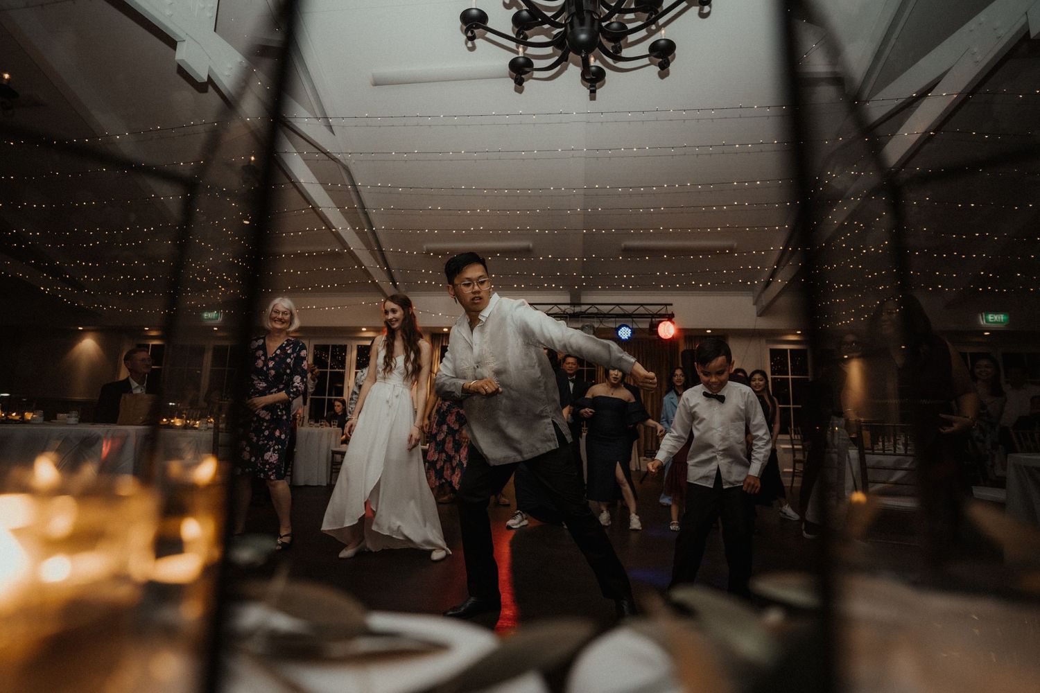 Wedding guests dance joyfully on the dance floor under a chandelier, with candlelit tables glowing in the foreground.