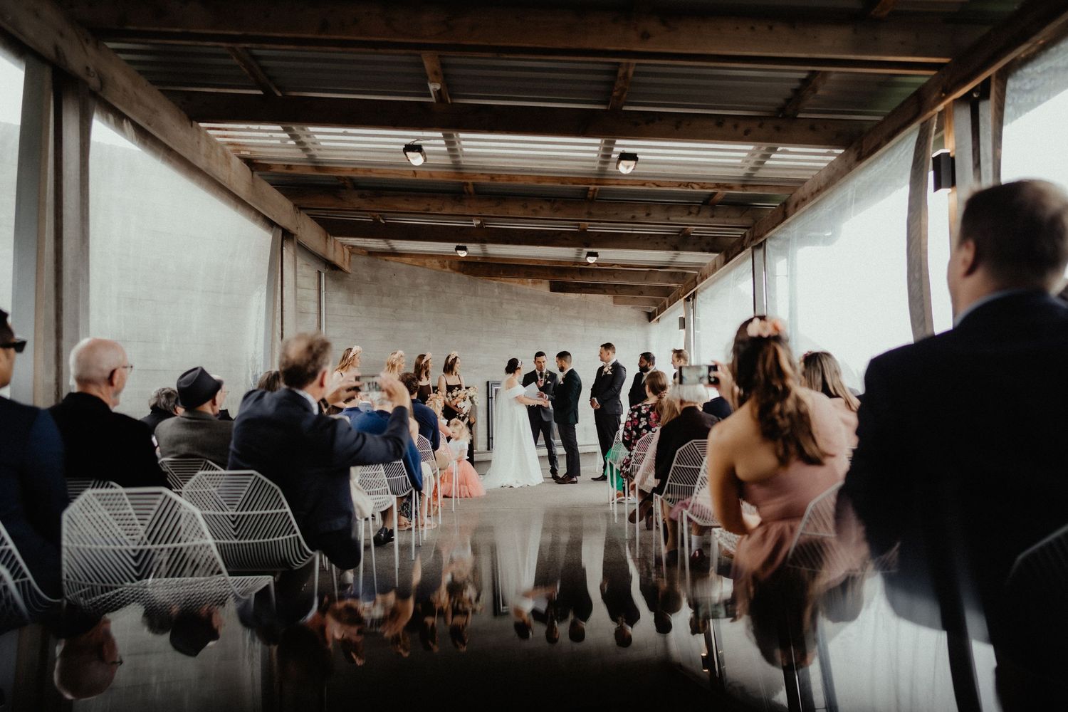 Wedding ceremony in a glass-walled venue as guests watch the bride and groom stand before the officiant.