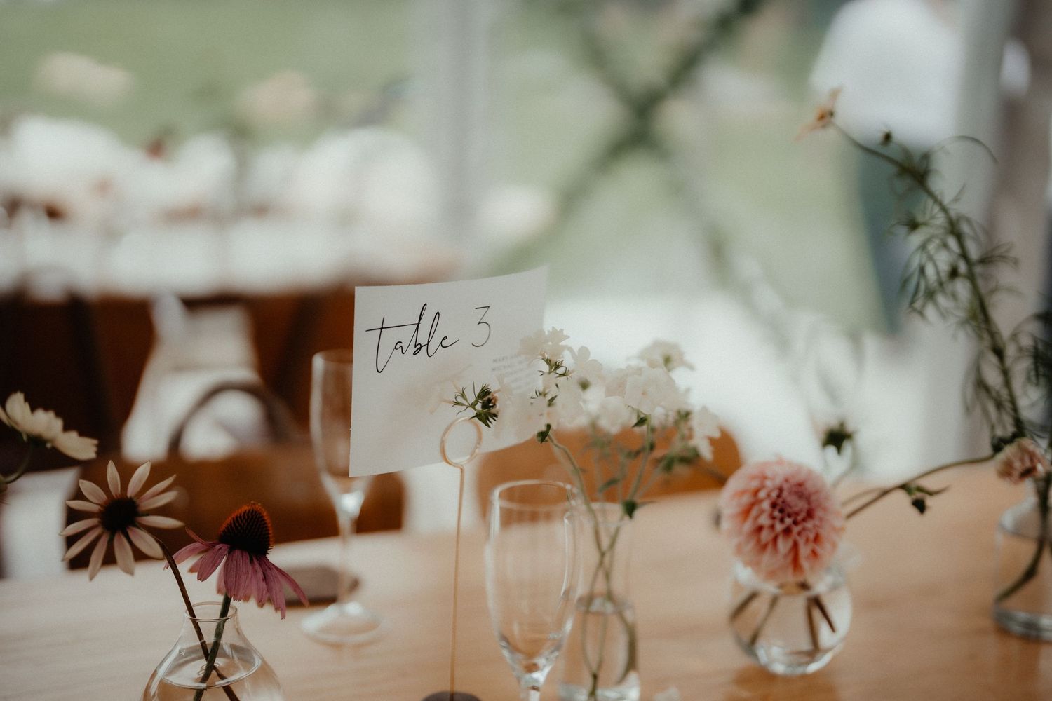 Wedding reception table with a table 1 sign, wine glasses and small vases of delicate pink and white flowers.