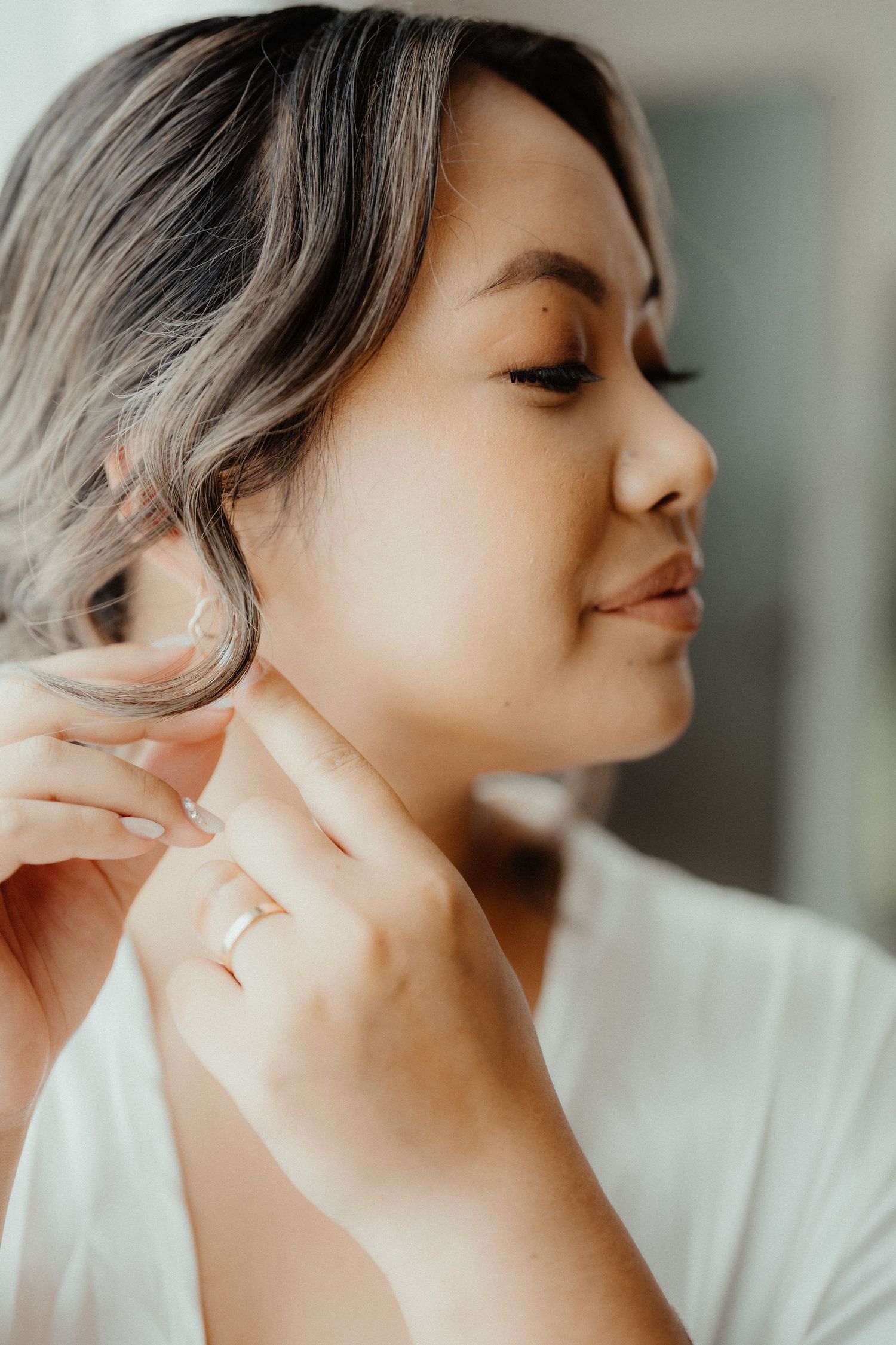 A woman in a white robe puts on an earring while getting ready for her wedding day.