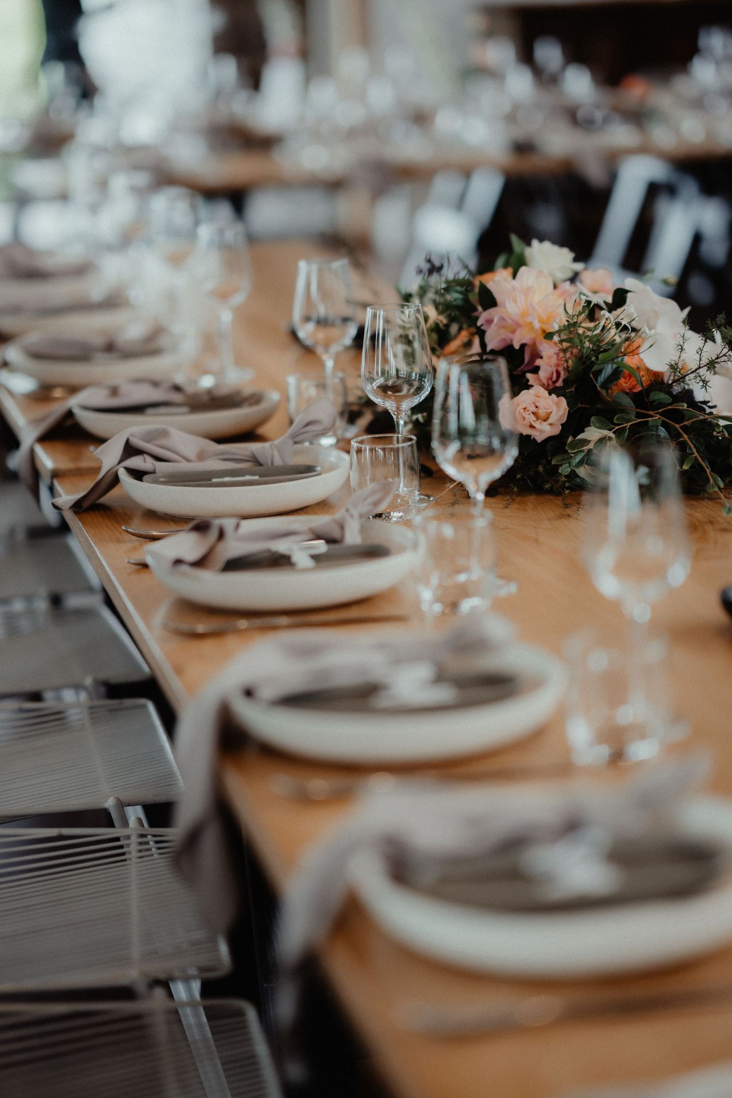 Close-up of a rustic wooden wedding table set with plates, napkins, glassware and a lush pink and white floral centerpiece.