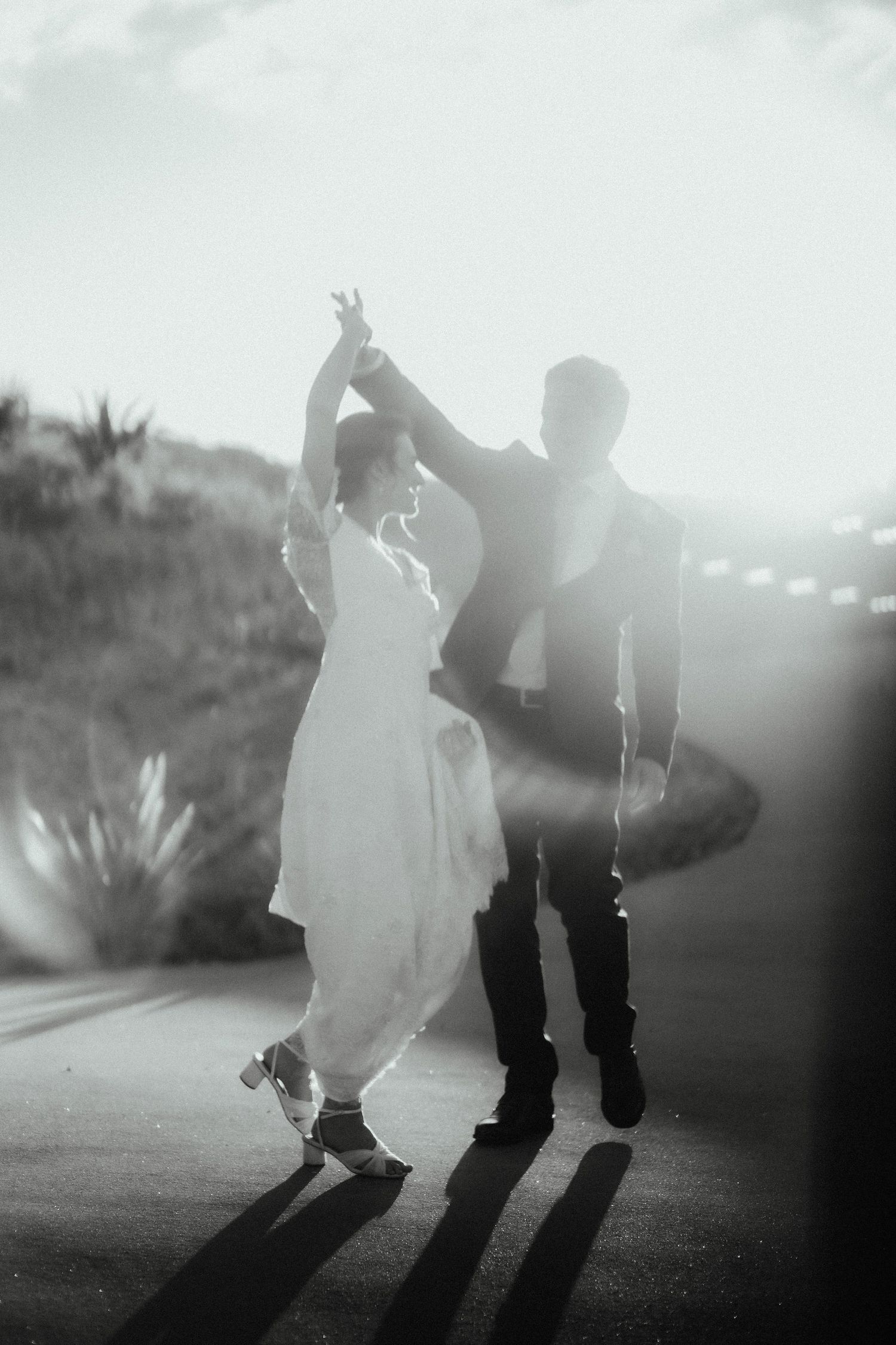 Black and white photo of a bride twirling under the raised arm of her groom in a backlit wedding dance.