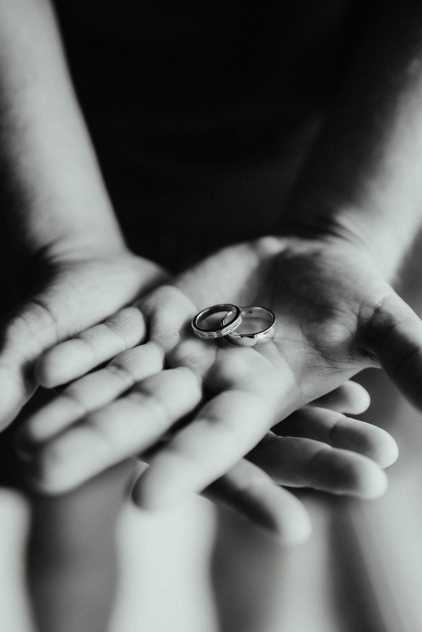 Black and white close-up of two wedding bands resting in a pair of cupped hands.