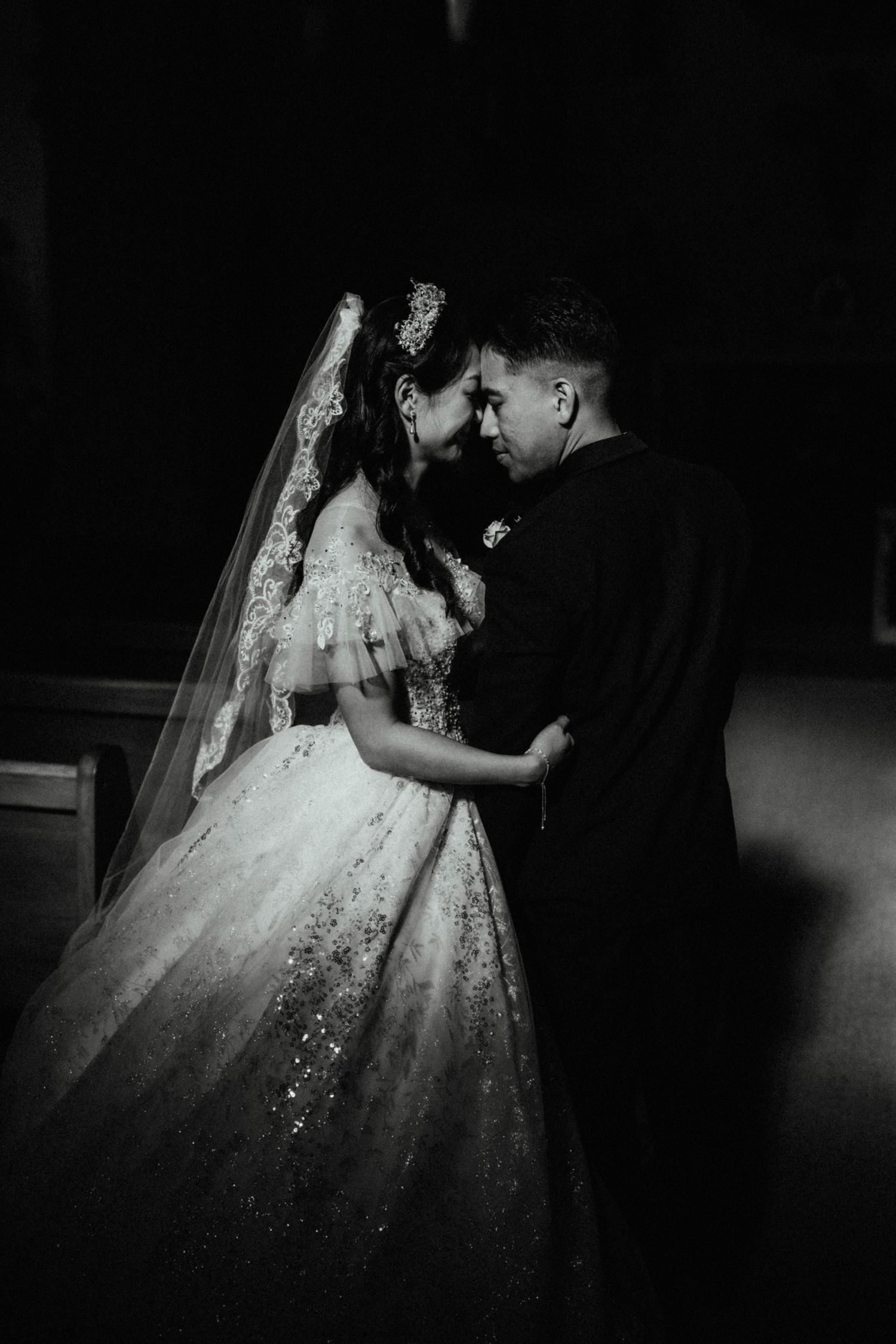Dramatic black and white photo of a bride in a sparkling ball gown and lace veil touching foreheads with her groom.